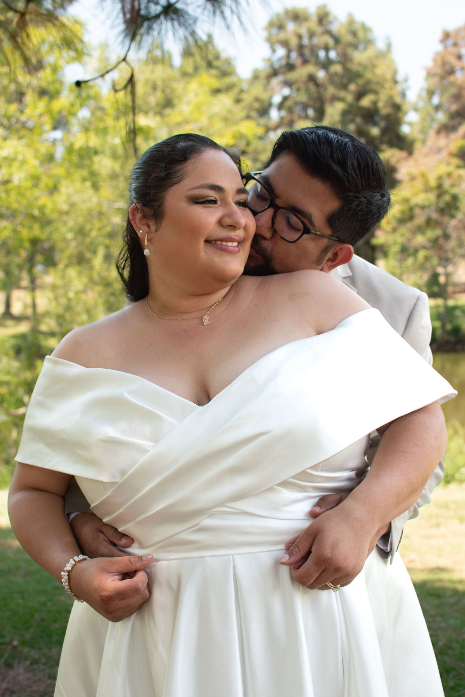 A romantic outdoor wedding portrait shows a couple embracing, with the bride wearing an elegant off-shoulder white dress.