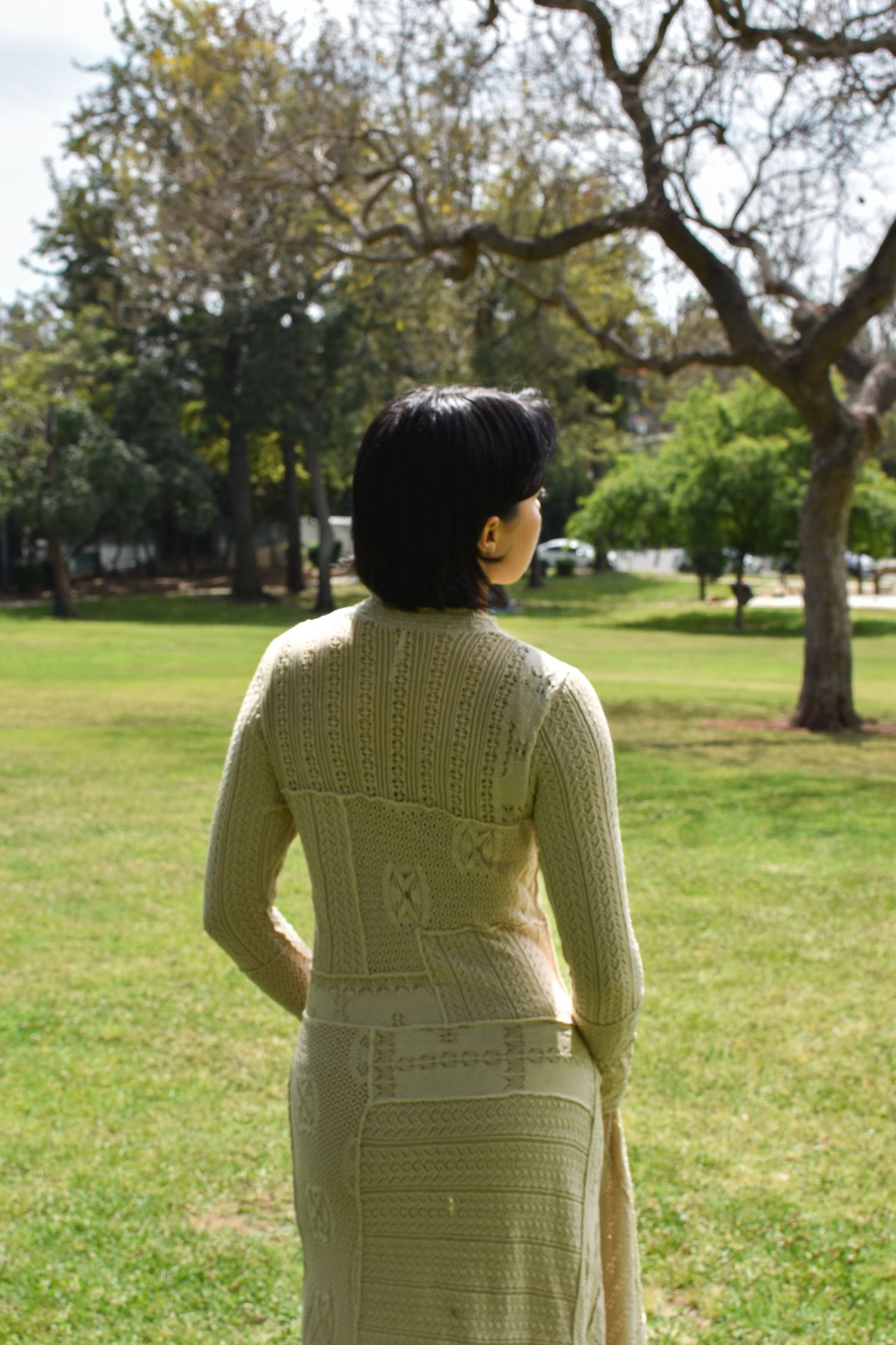 Back view of a detailed cream knit dress in a park setting.