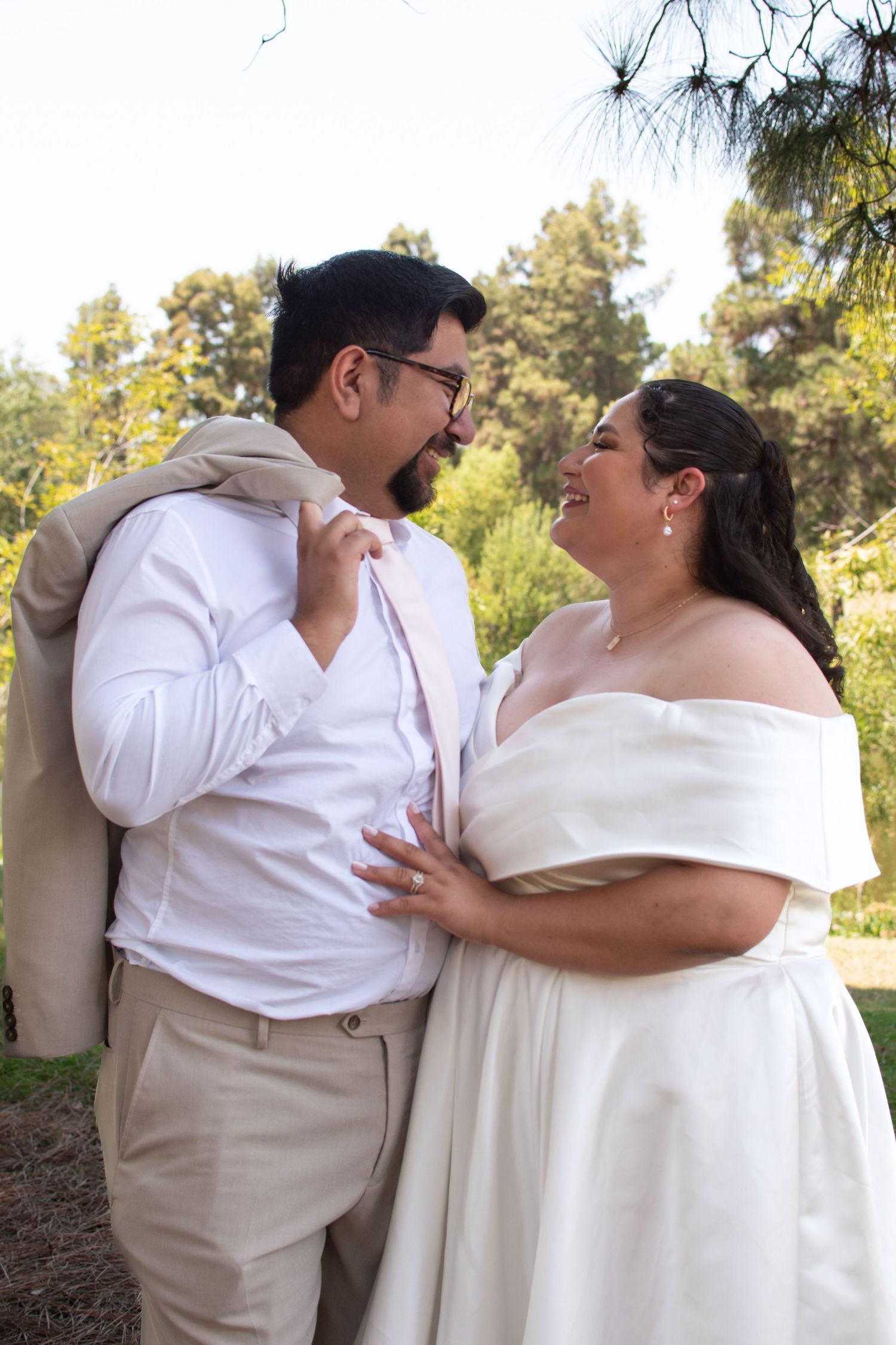A joyful couple shares a tender moment outdoors on their wedding day, dressed in elegant beige and white attire.