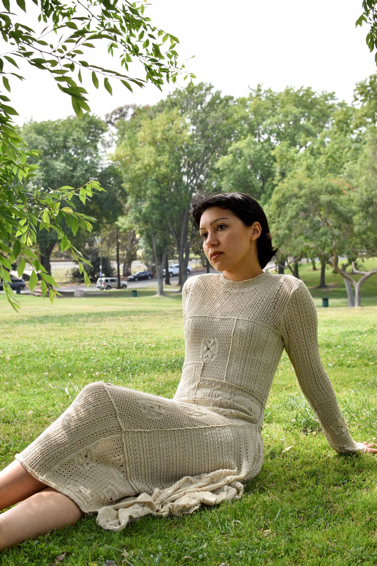 Model in cream knit dress poses on grass in a park setting.
