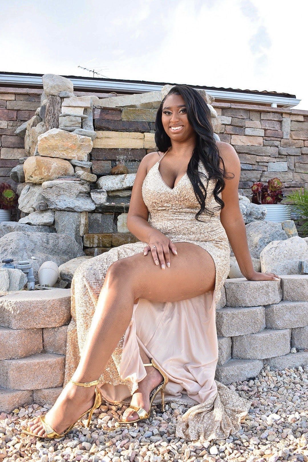 Glamorous formal photoshoot by stone waterfall feature in sequined dress.