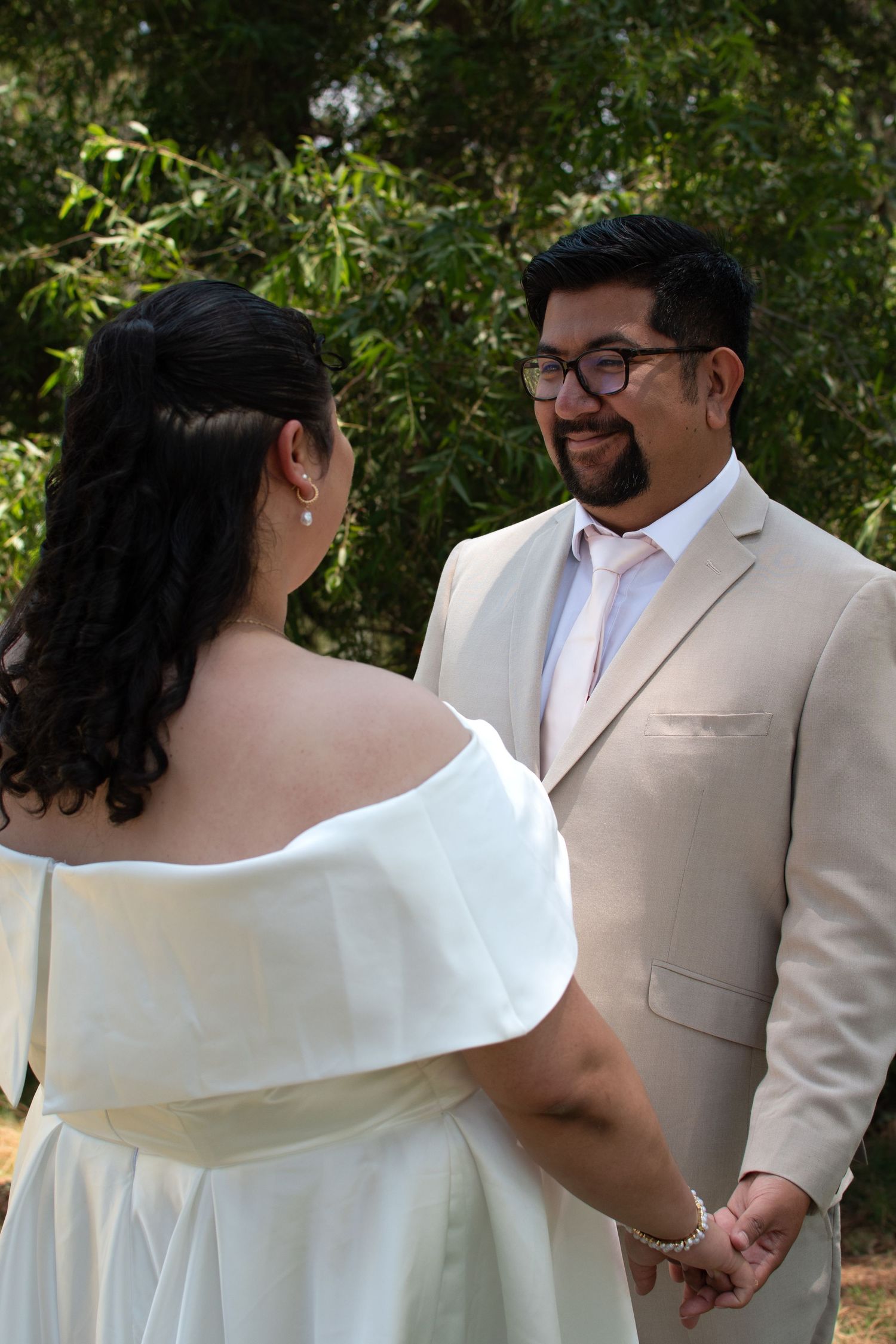 A couple shares a tender moment during their outdoor wedding ceremony on a sunny day in a garden setting.