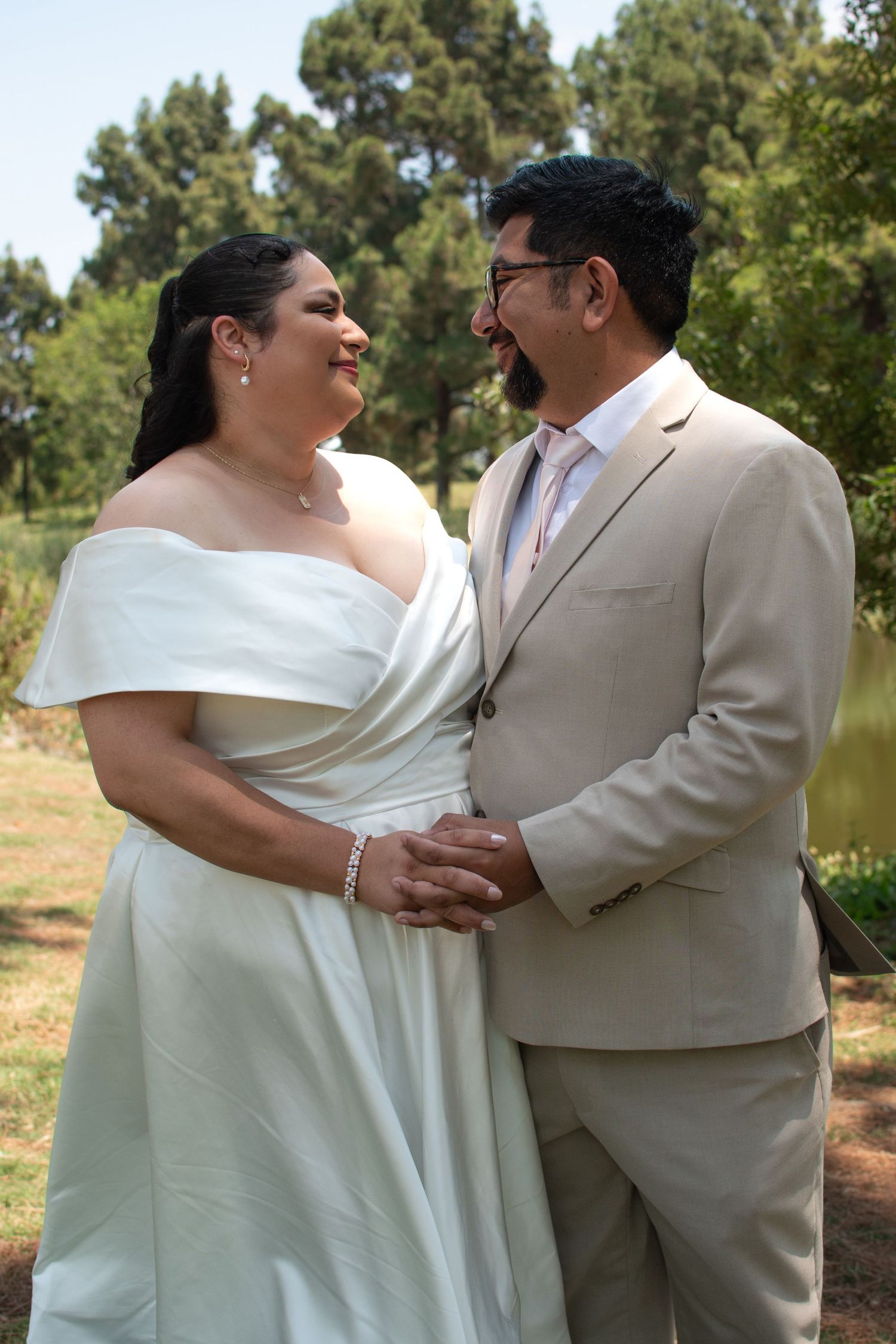 Happy couple in white dress and tan suit embracing and laughing together in an outdoor woodland setting.
