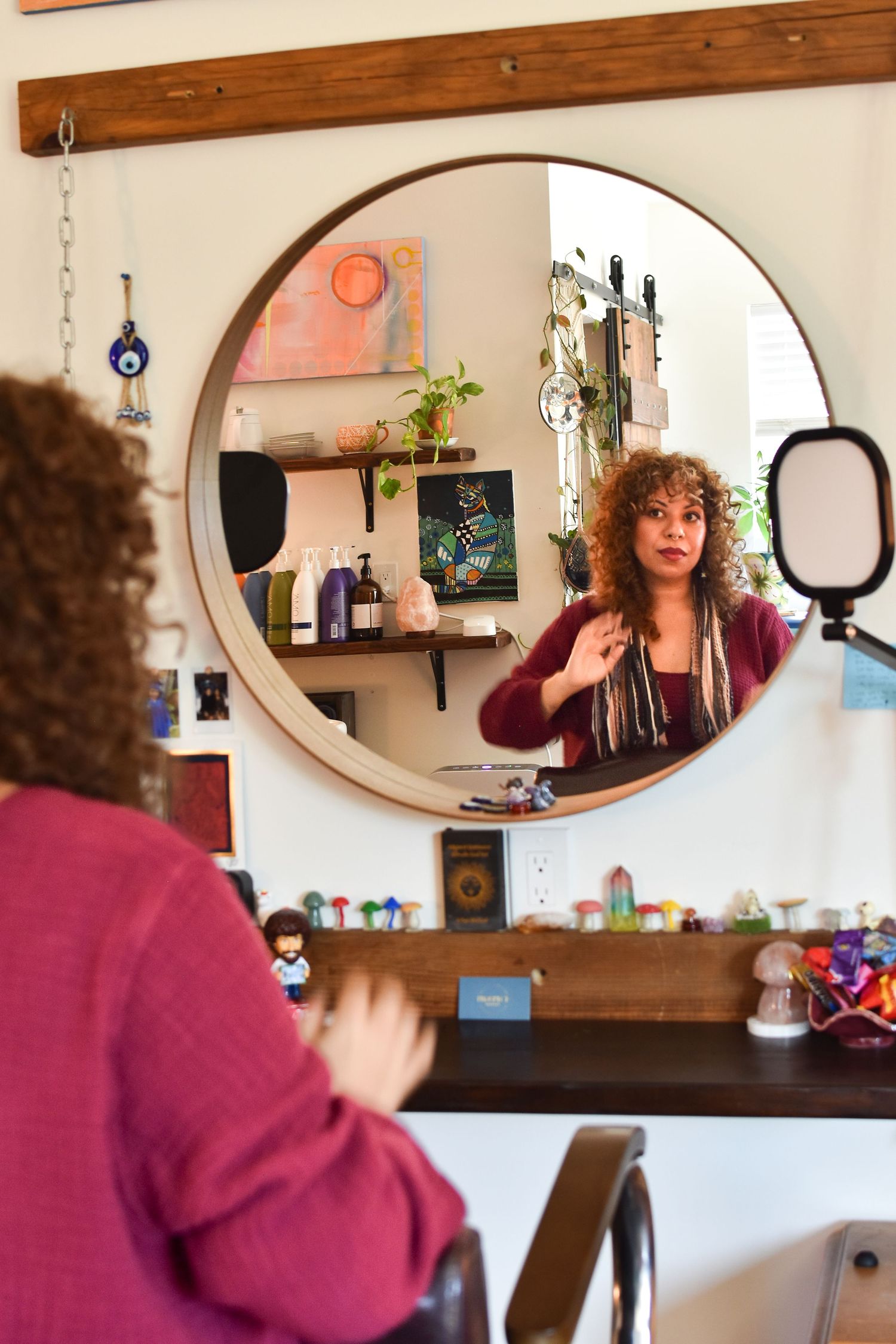Reflection in circular mirror shows a cozy salon interior with wooden shelving and decorative items on display.