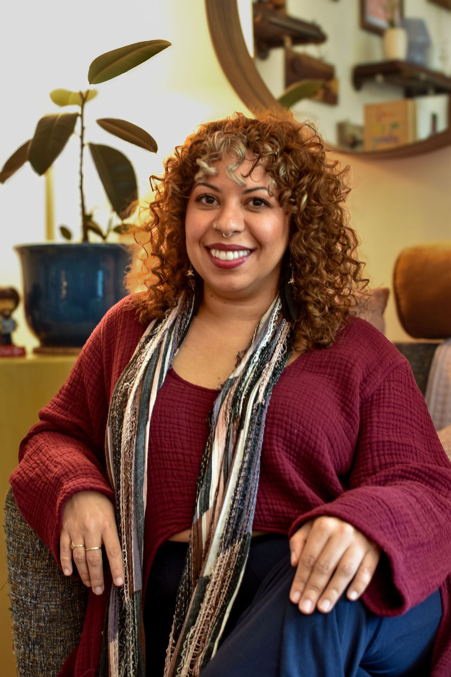 An indoor portrait showing a burgundy sweater and decorative scarf while sitting in a cozy living room setting.