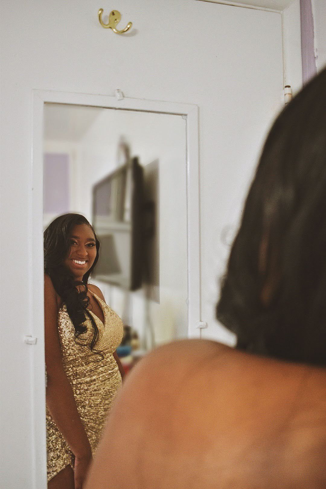 Mirror reflection shows a joyful moment in a sparkly gold evening gown.
