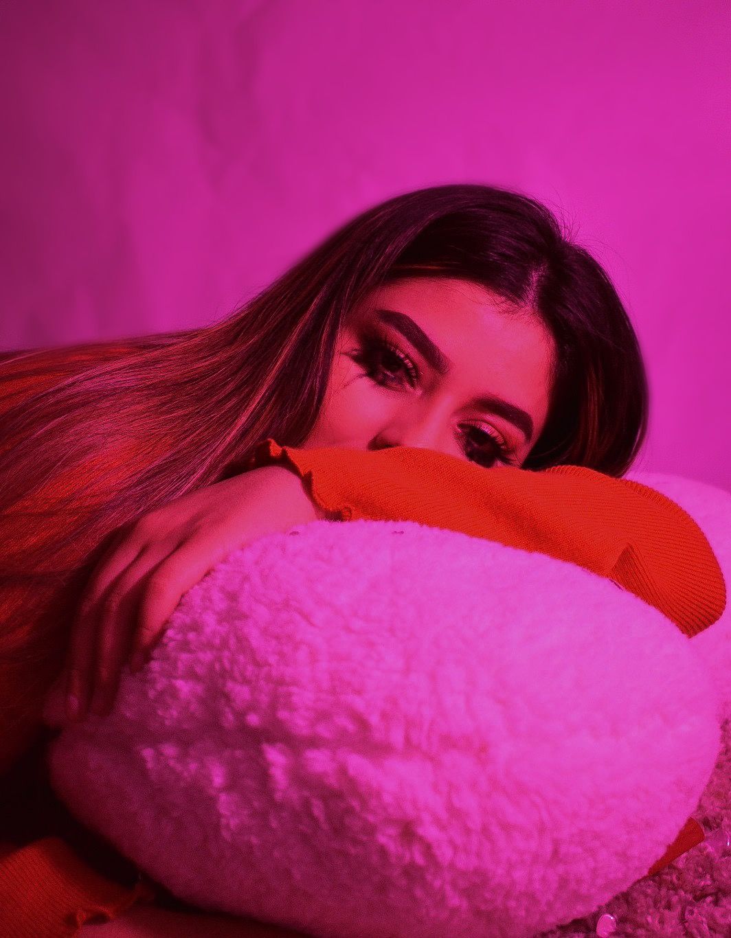 Artistic portrait with pink lighting showing person hugging plush pillow.