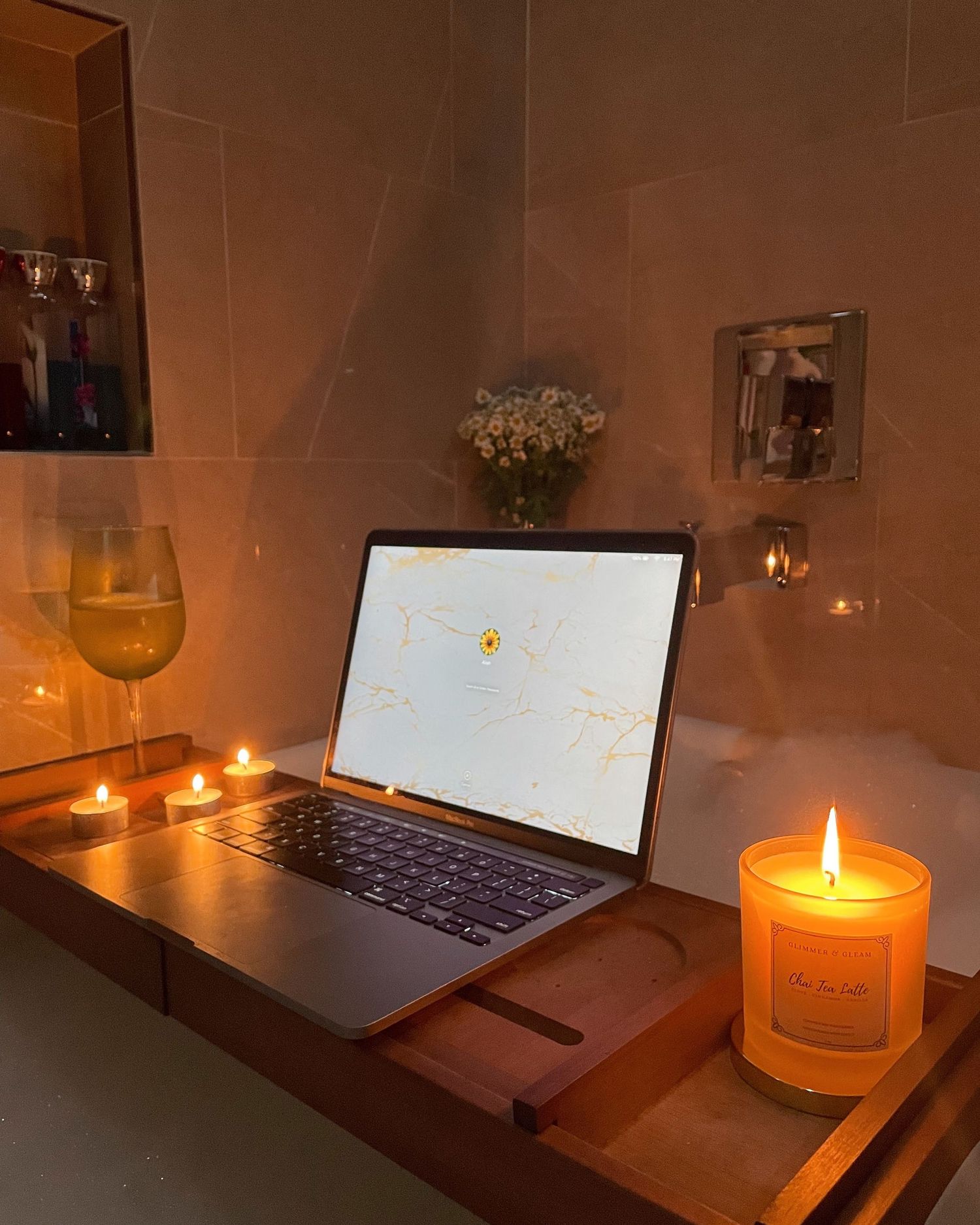 Cozy evening workspace with laptop, candles, and wine glass in warm ambient lighting.