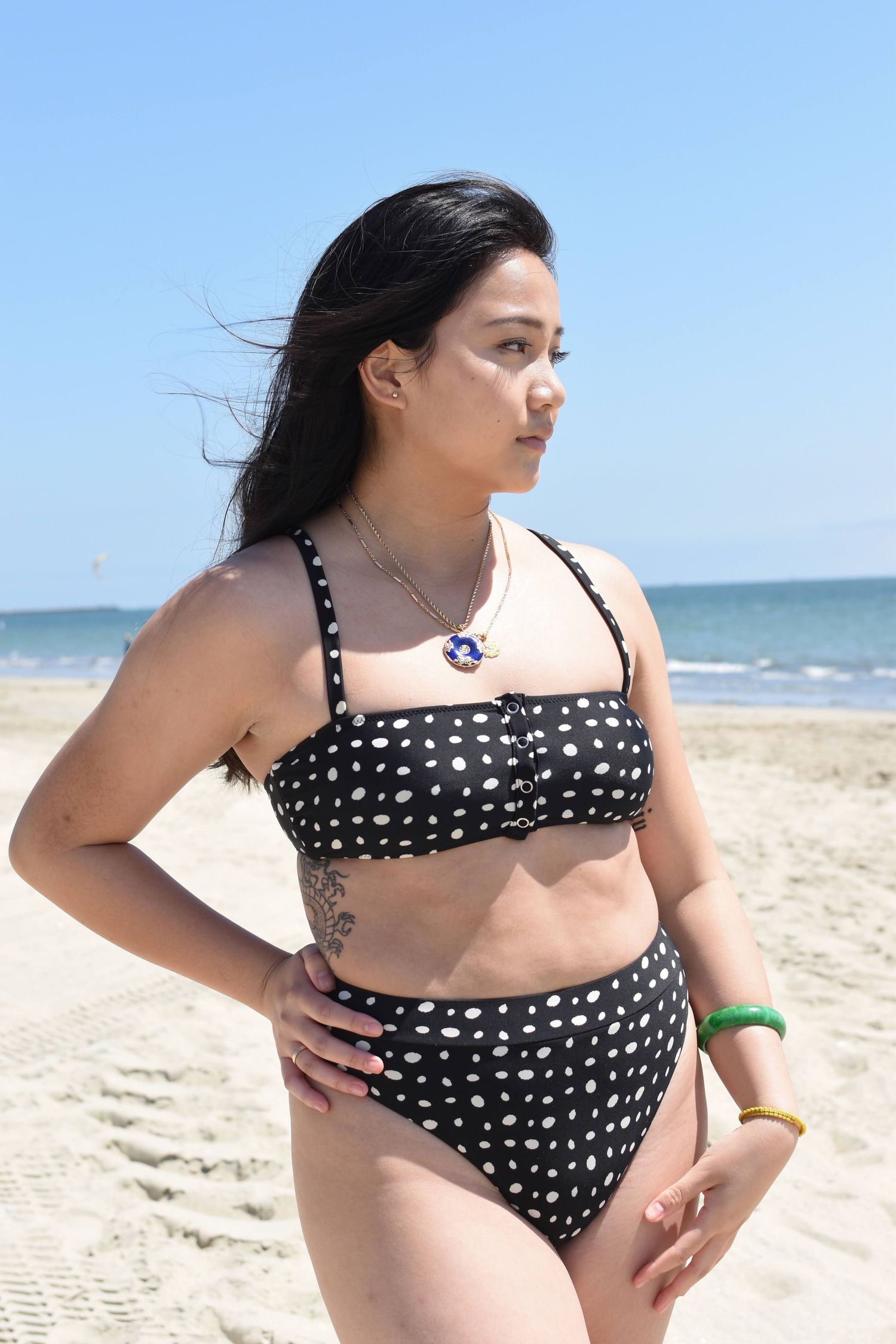 Person in polka dot bikini standing on beach with ocean in background.