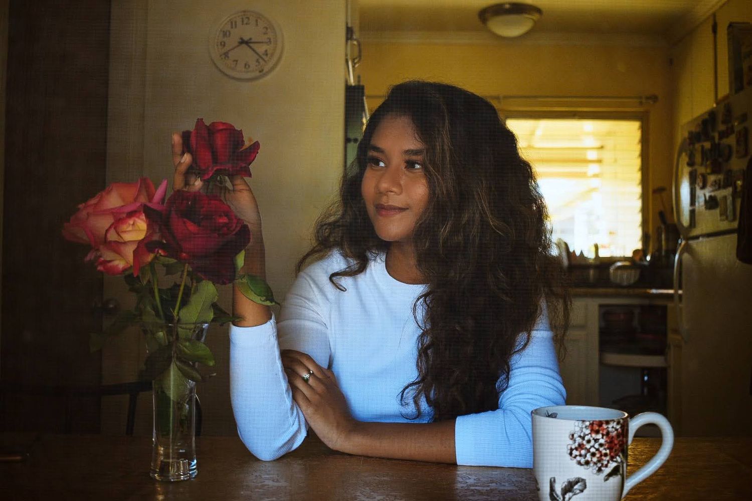 Person at wooden table with decorated mug and red roses in indoor setting.
