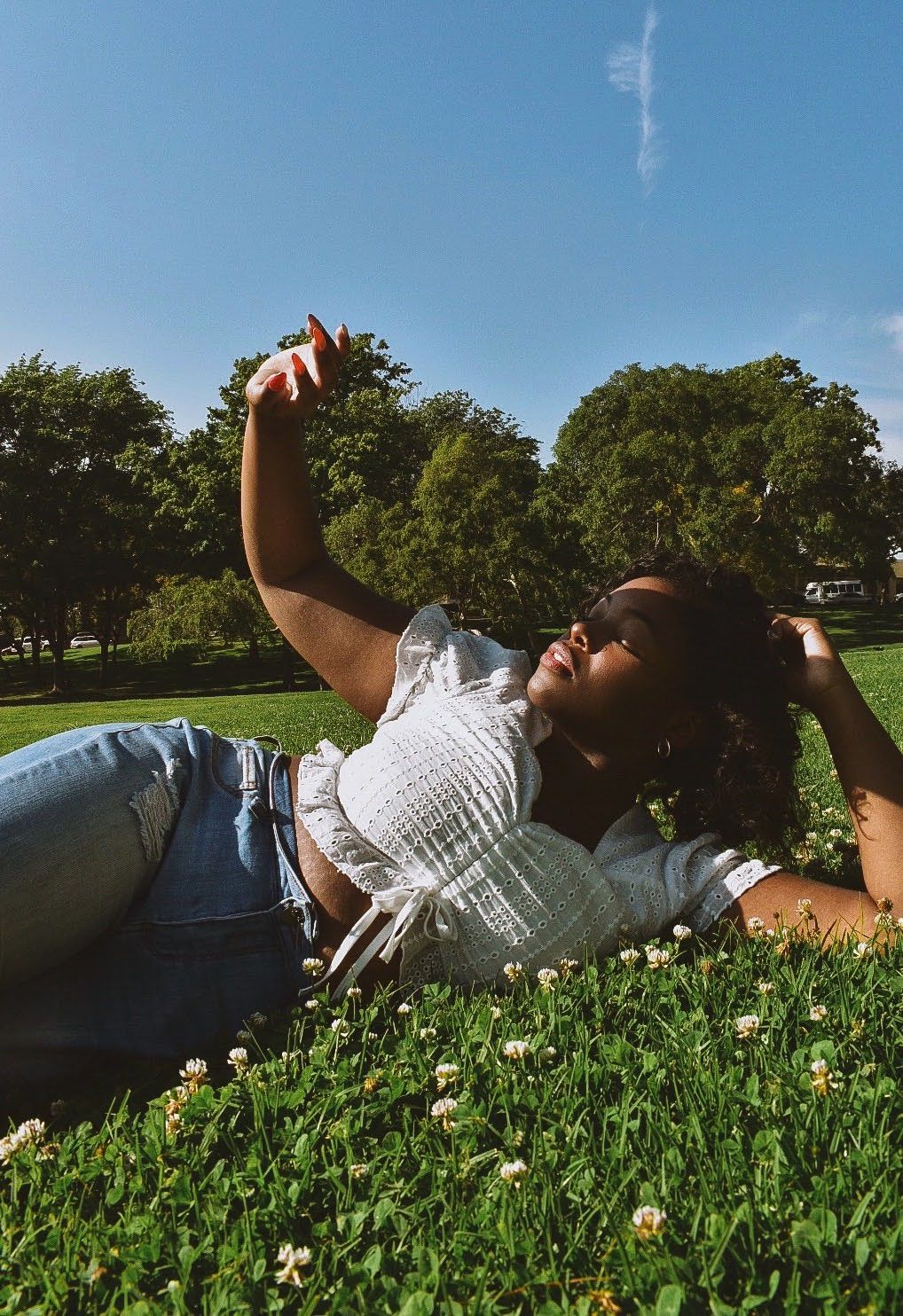Relaxed summer portrait lying in grass with white top and jeans under blue sky.