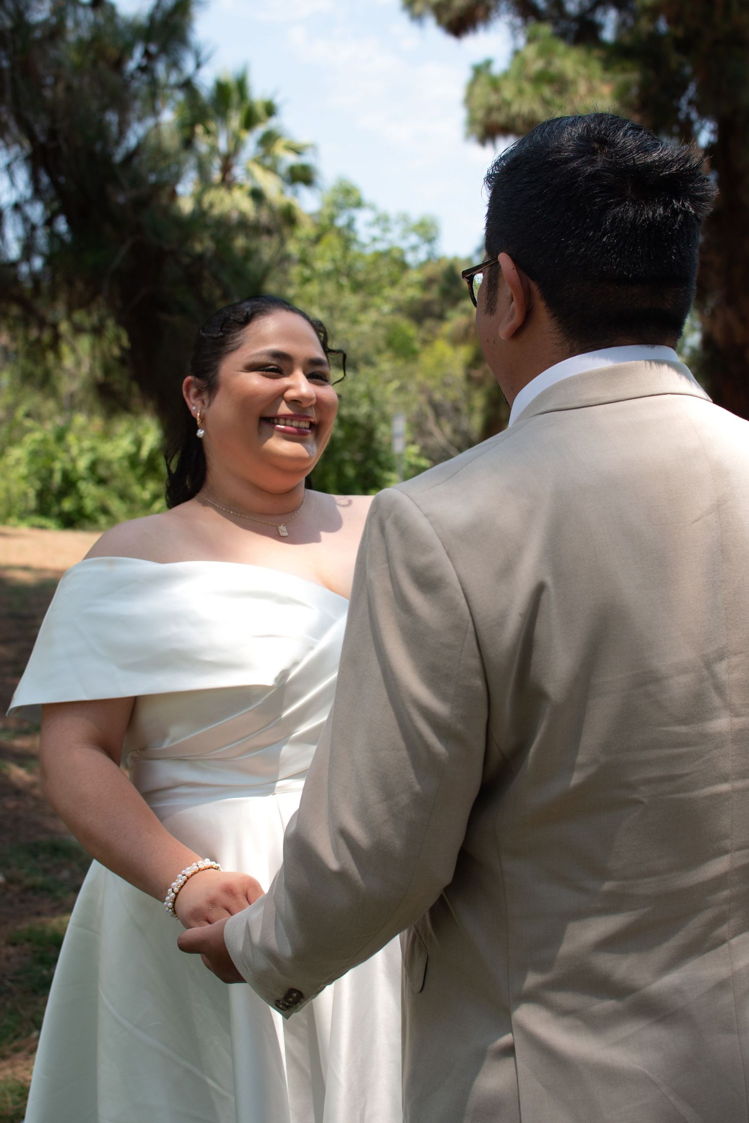 A joyful outdoor wedding moment showing a couple in white and beige formal attire sharing a candid laugh together.