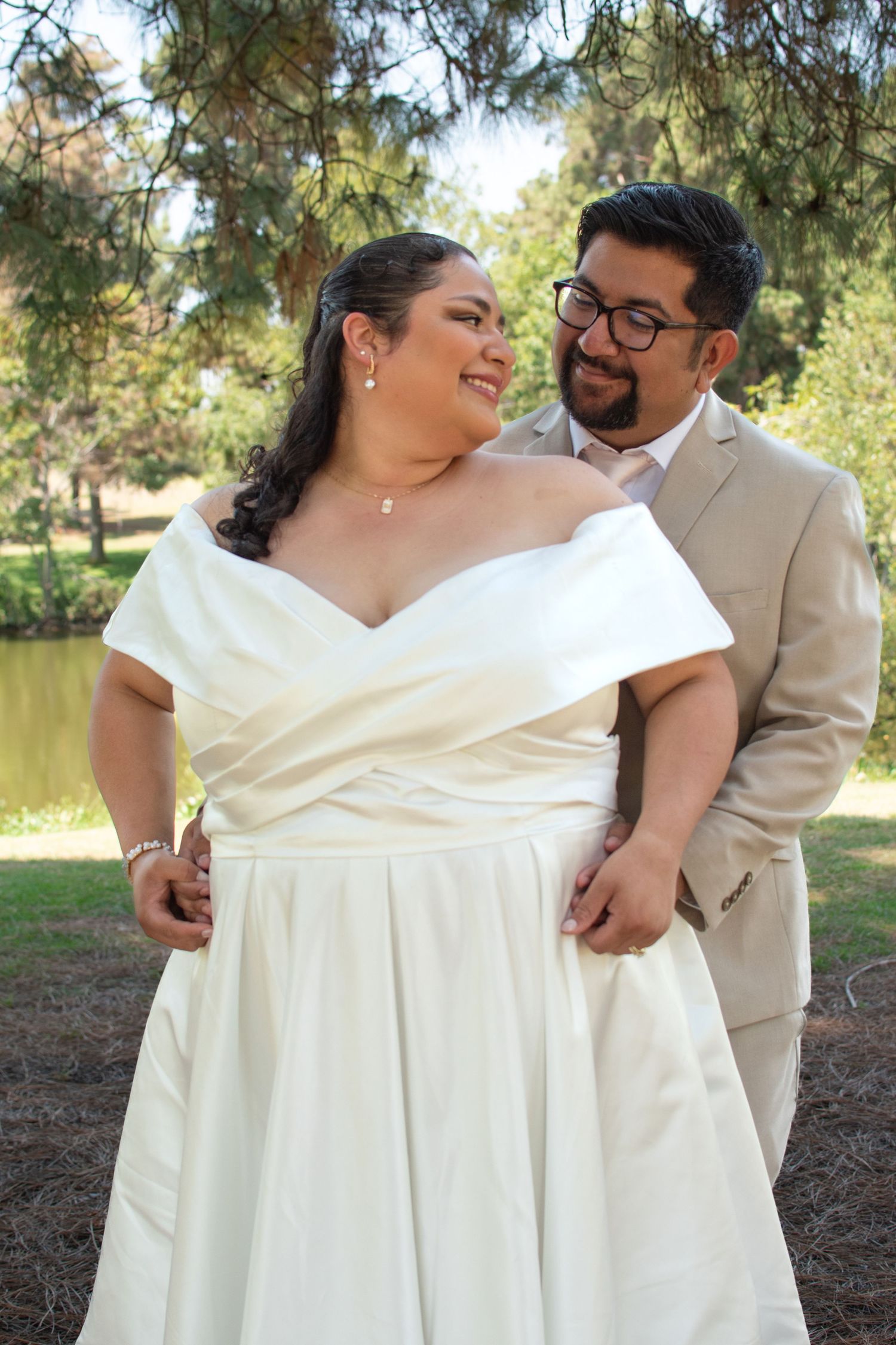 A newlywed couple in beige and white outfits share joyful laughter during their outdoor wedding photoshoot.