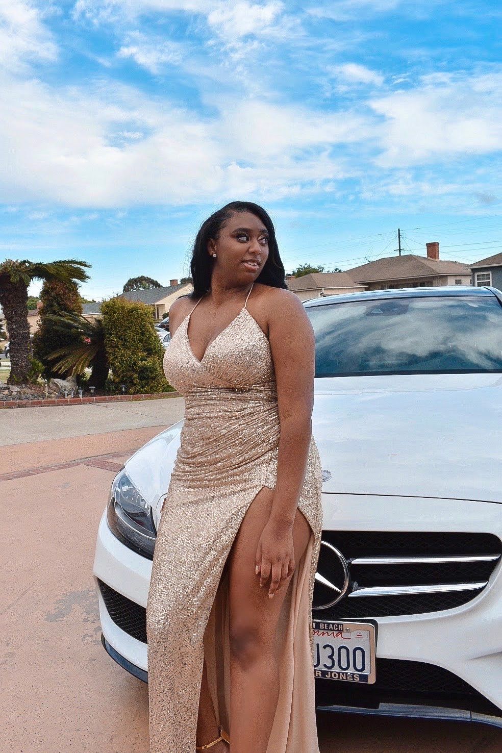 Sophisticated champagne sequin dress photographed against white luxury car and blue sky.