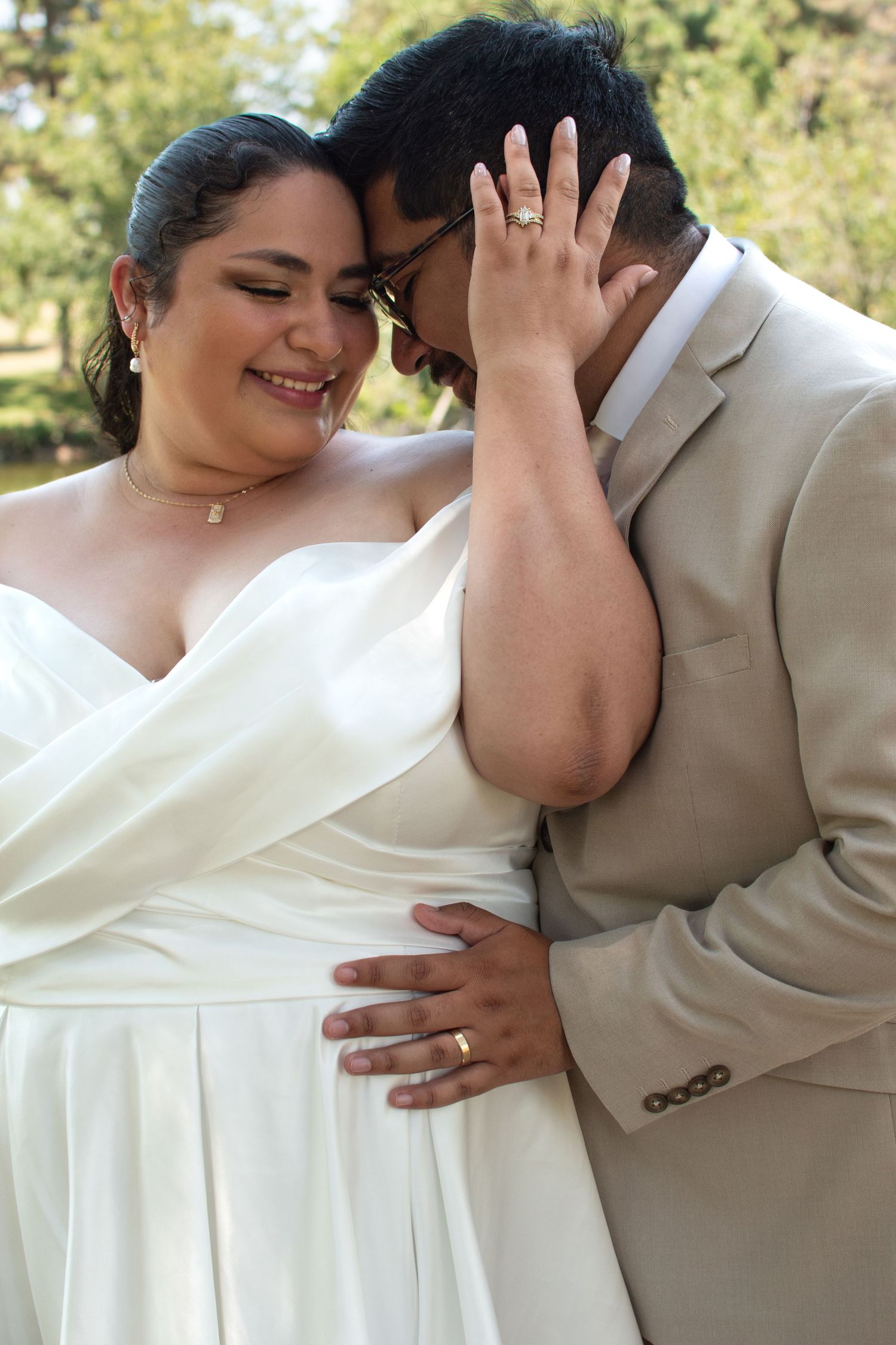 A tender wedding moment between a couple in formal attire sharing an intimate embrace outdoors.