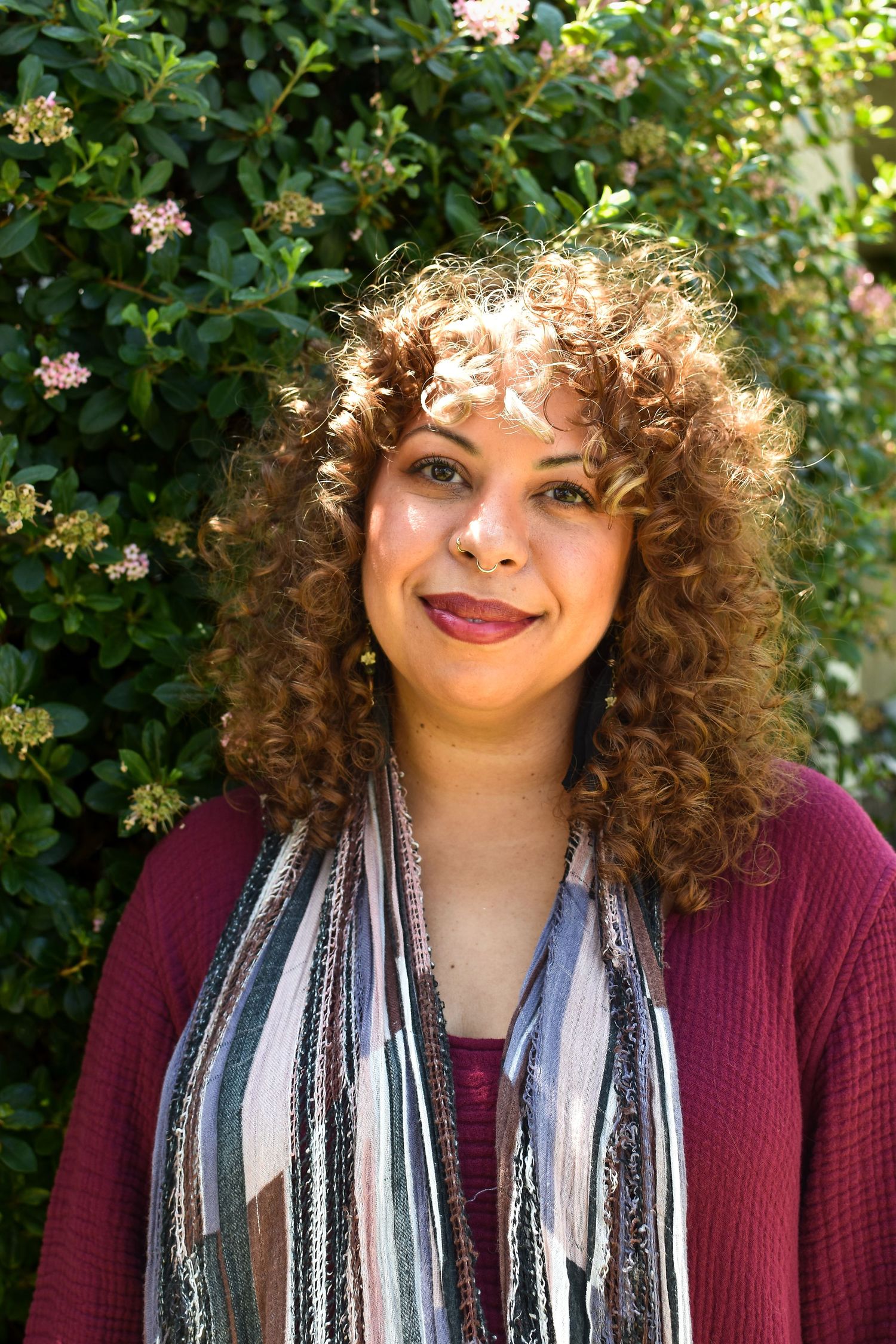 A series of similar fashion portraits showing someone wearing a burgundy sweater and striped scarf in front of green foliage.