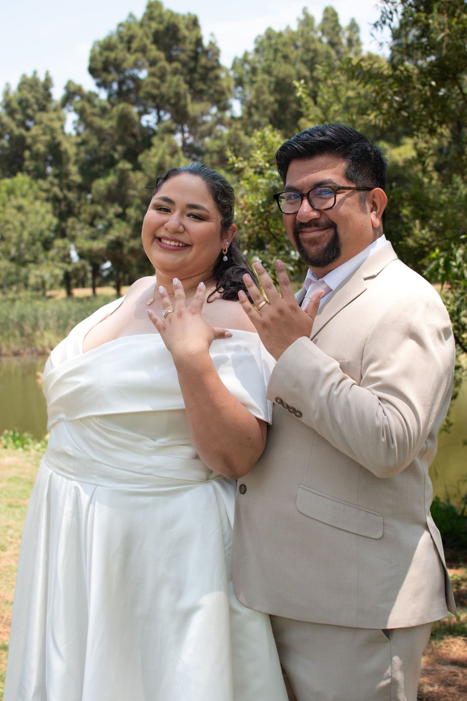 A couple in wedding attire share a joyful dance embrace outdoors with trees in the background.