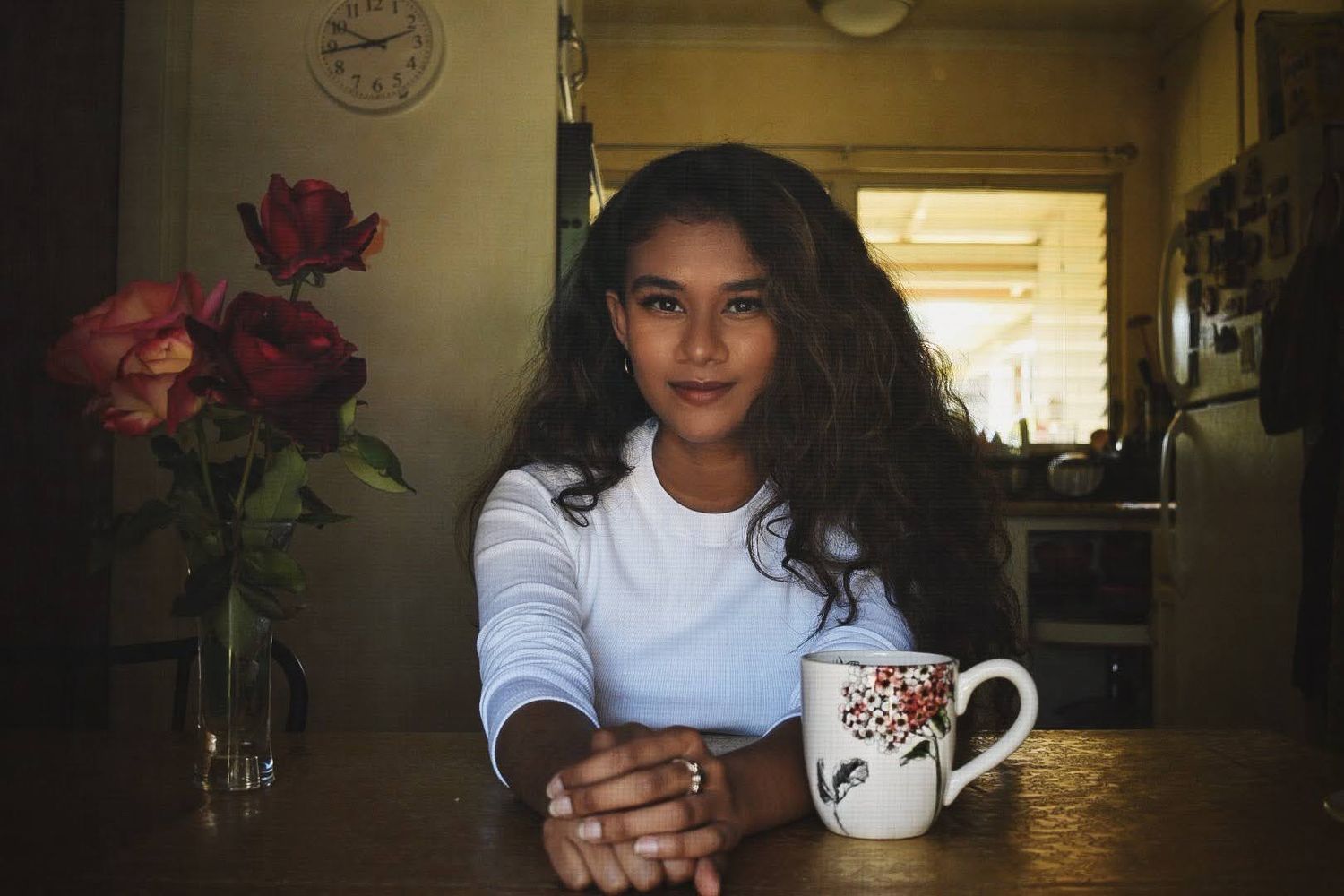 Person sitting at wooden table with patterned mug in warm indoor setting.