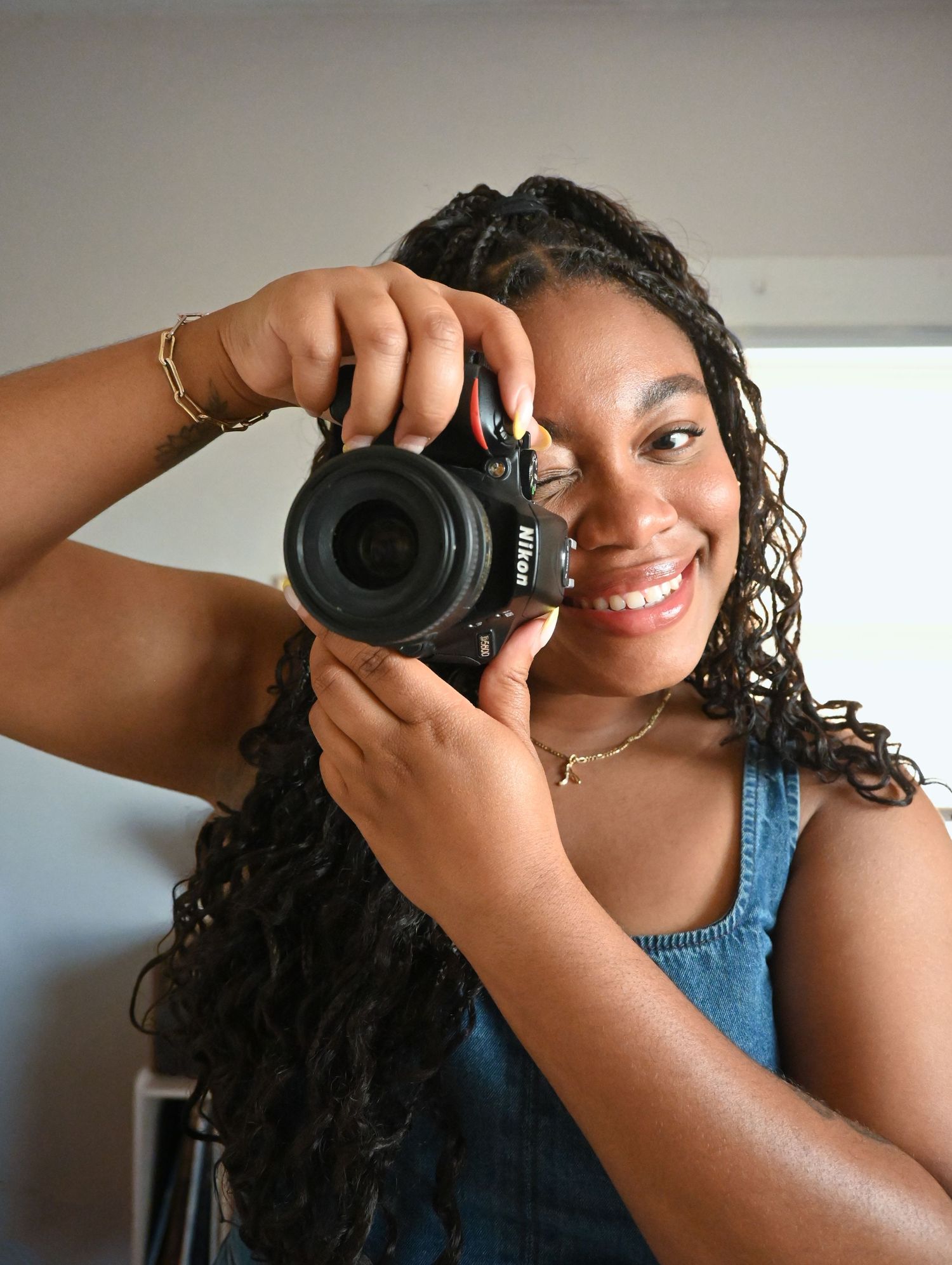 A creative self-portrait of a photographer holding a professional camera and wearing delicate jewelry.
