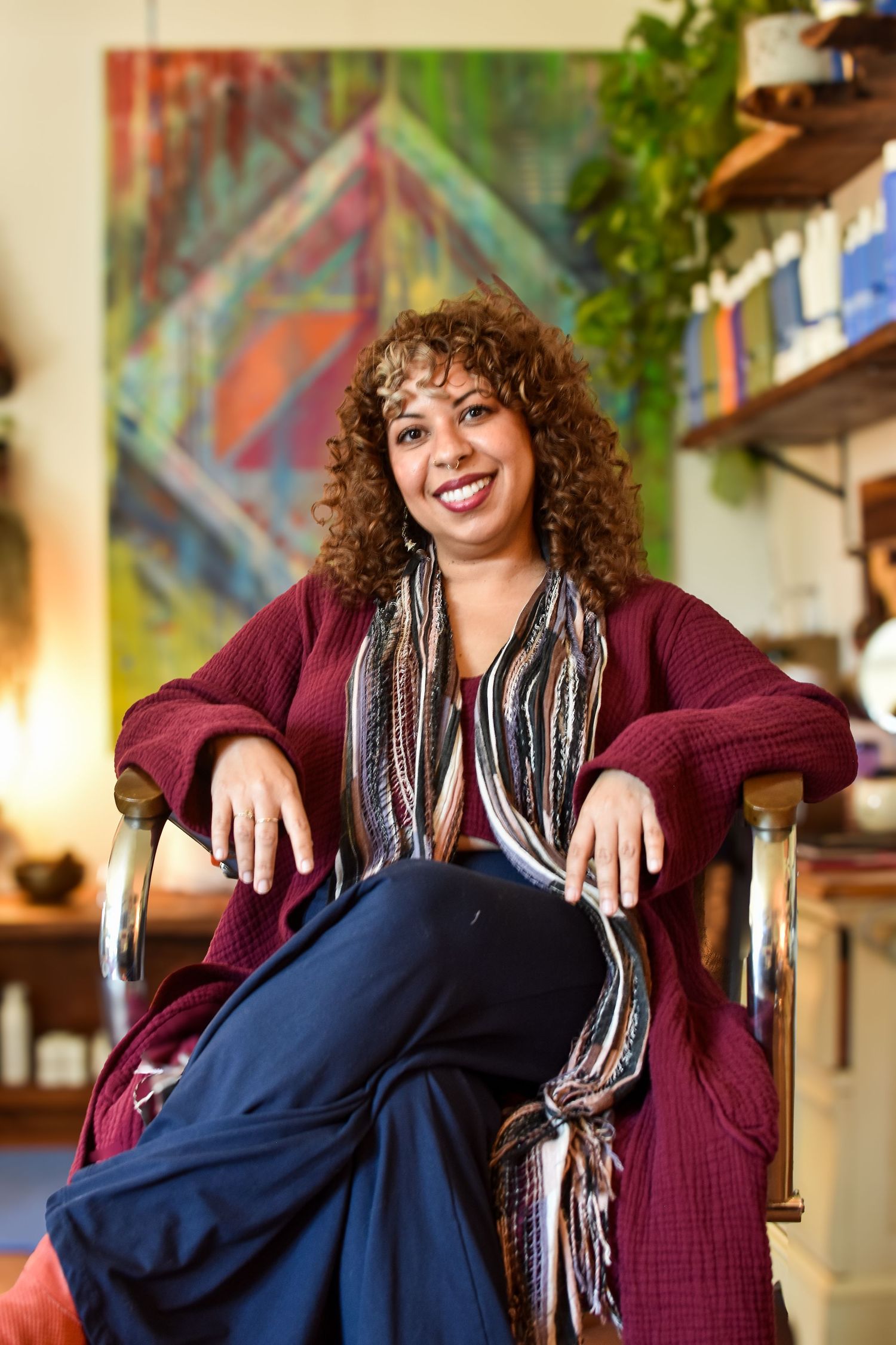 A person wearing a maroon cardigan, striped shirt and dark pants is shown sitting comfortably in a chair indoors.
