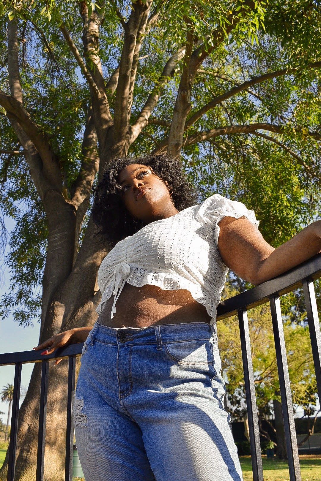 Low angle shot showing white summer top and denim against leafy tree backdrop.