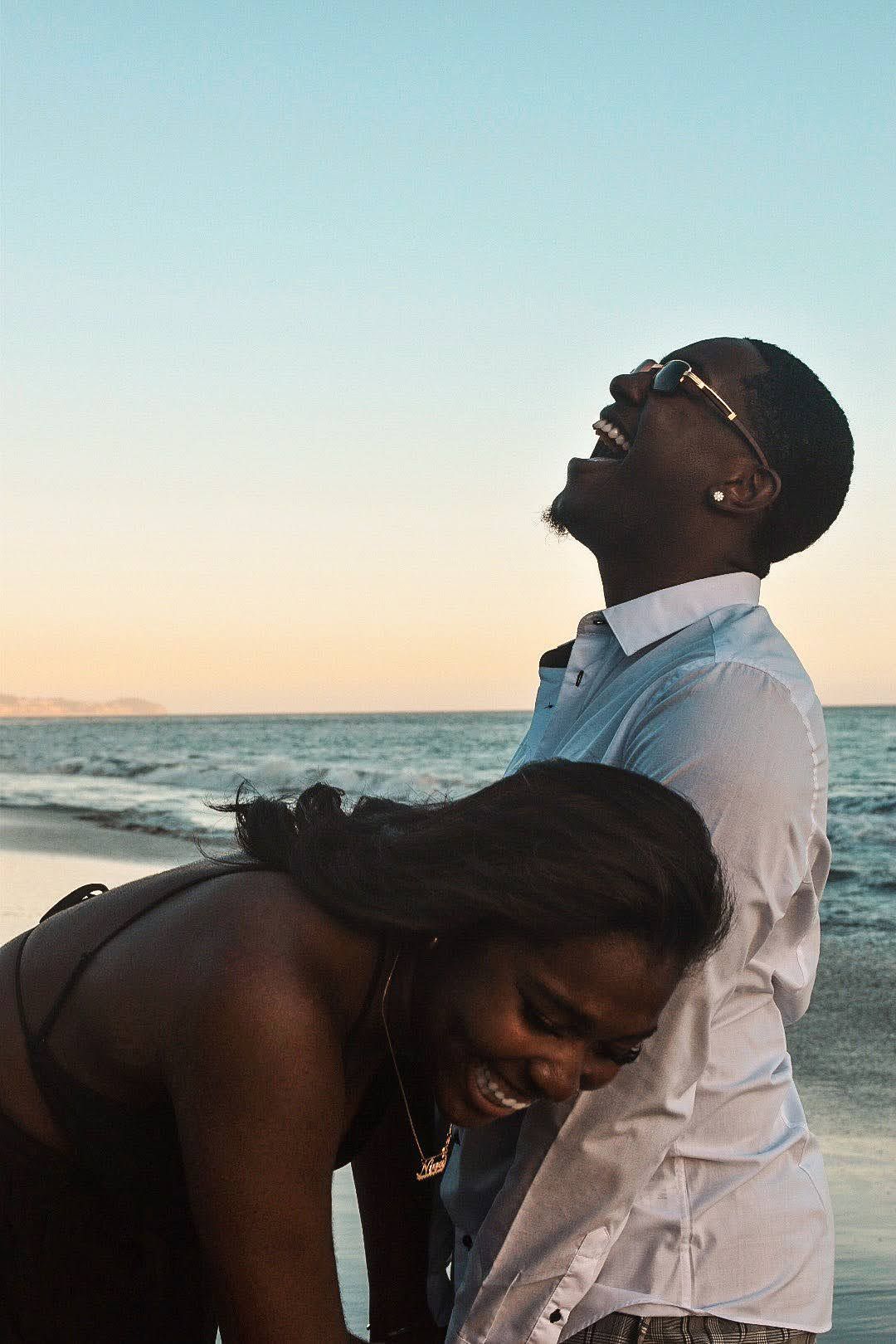 Intimate candid moment of couple sharing laughter on beach during golden hour.
