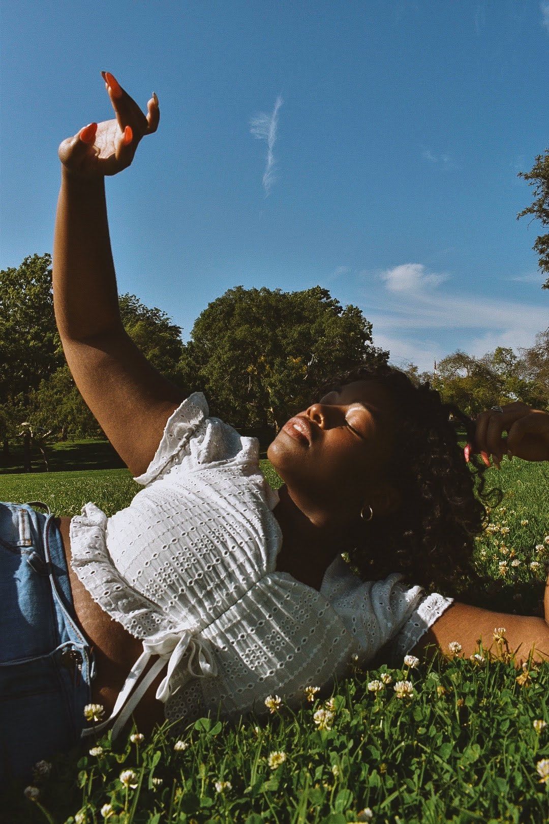 Candid summer photo lying in flowering grass wearing white top and denim.