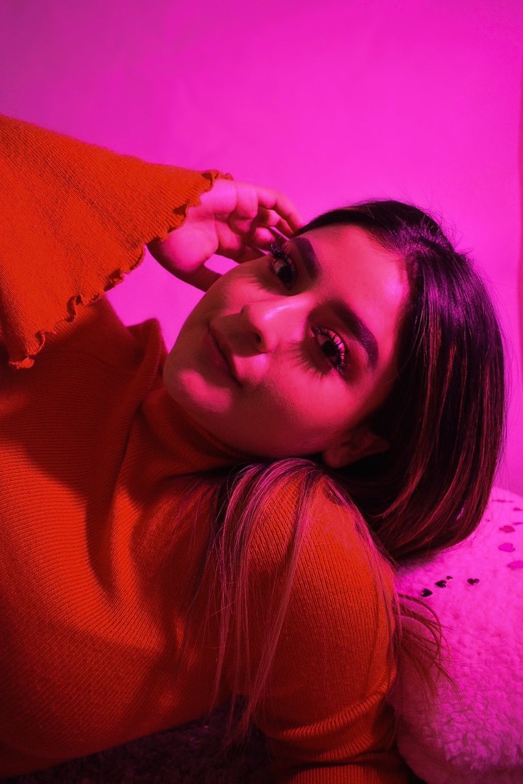 Stylized close-up portrait with pink lighting and red sweater creating emotional atmosphere.