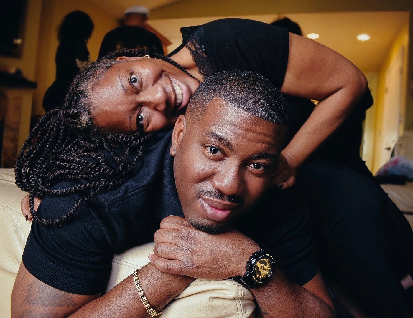 A joyful mother and her son poses together indoors with playful expressions and casual black attire.
