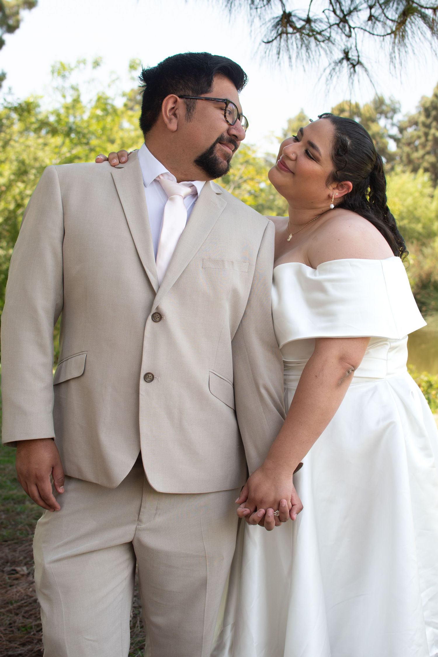 A bride and groom in light beige and white attire share an intimate moment outdoors during their wedding photoshoot.