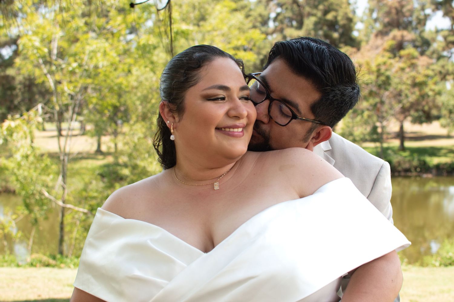 A loving embrace between a couple in wedding attire standing beside a scenic pond on their special day.