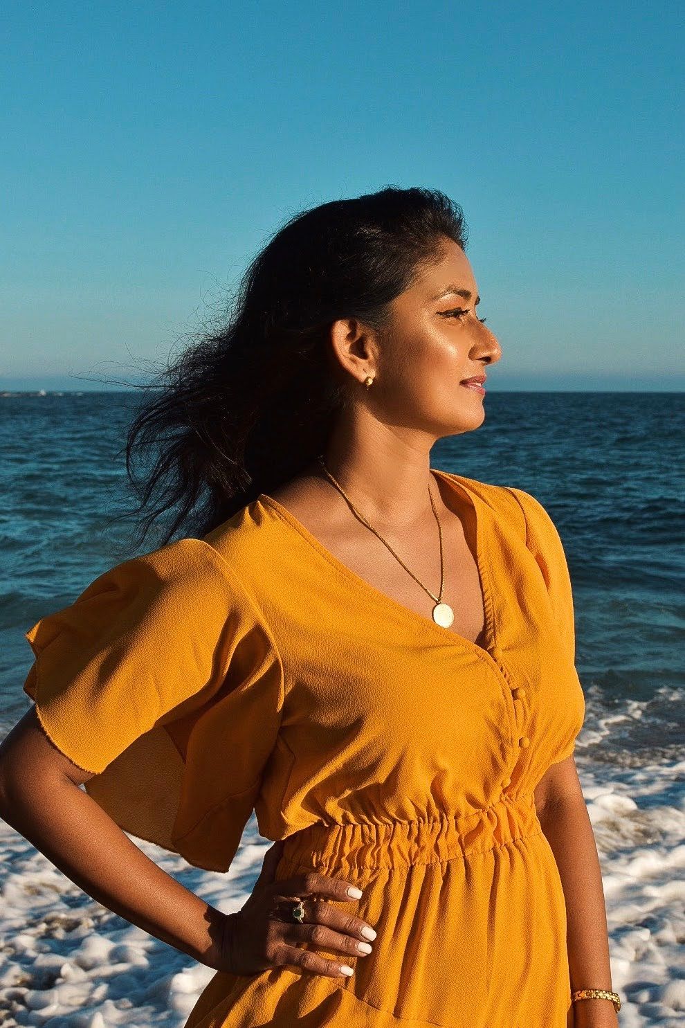 A person wearing a yellow summer dress stands against a backdrop of blue ocean waves.