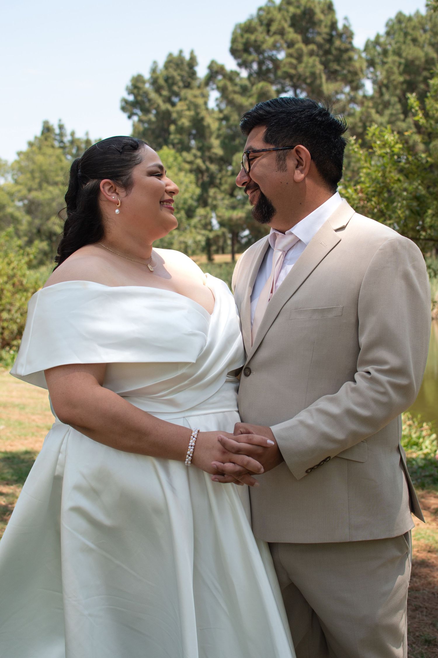 Happy couple sharing a joyful moment together outdoors on their wedding day in white dress and beige suit.