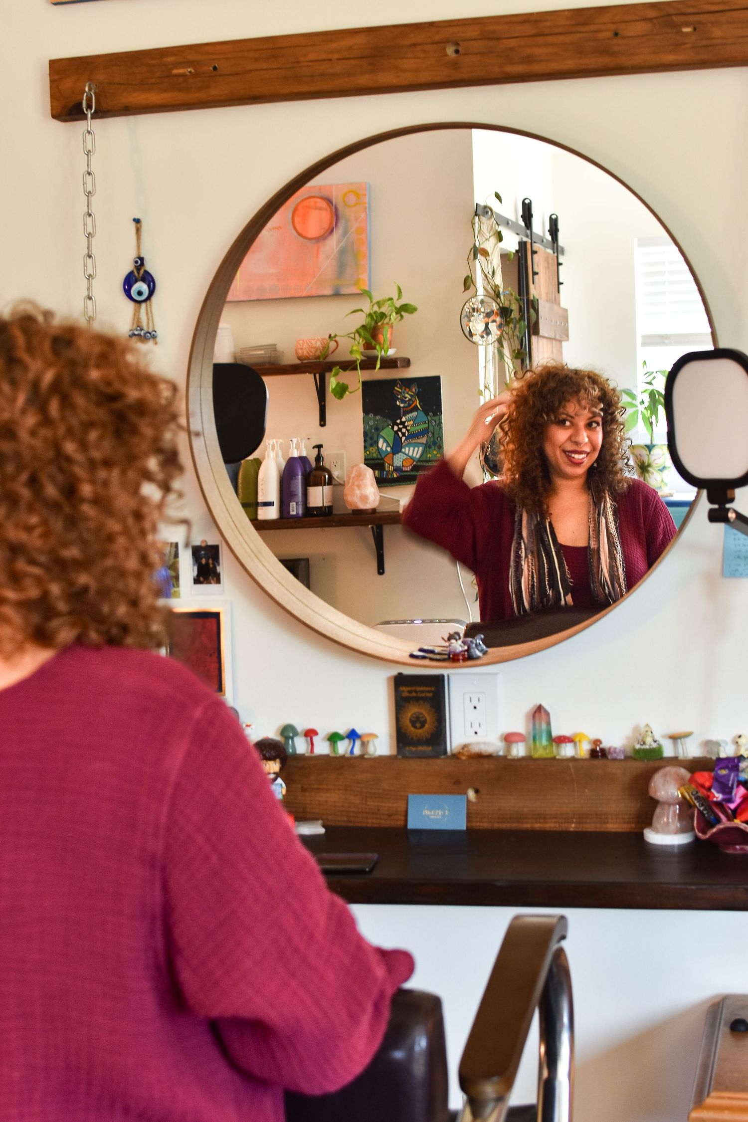 A person sits at a vanity mirror in a home interior with warm wood tones and burgundy accents.