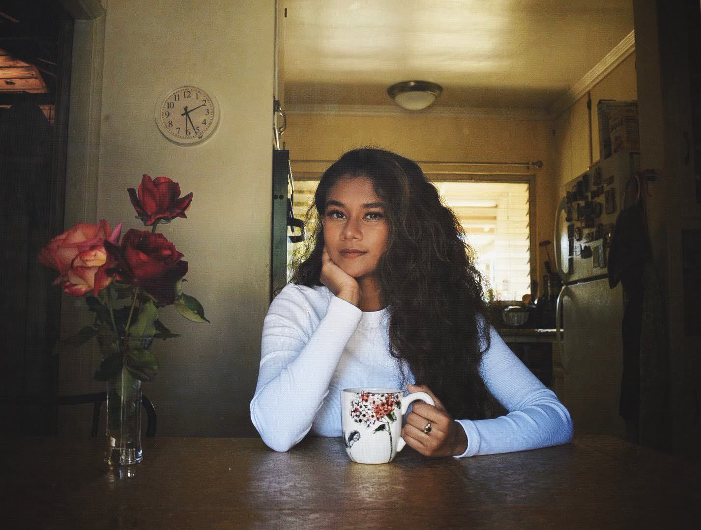 Person sitting with decorative mug at wooden table in dim indoor lighting.