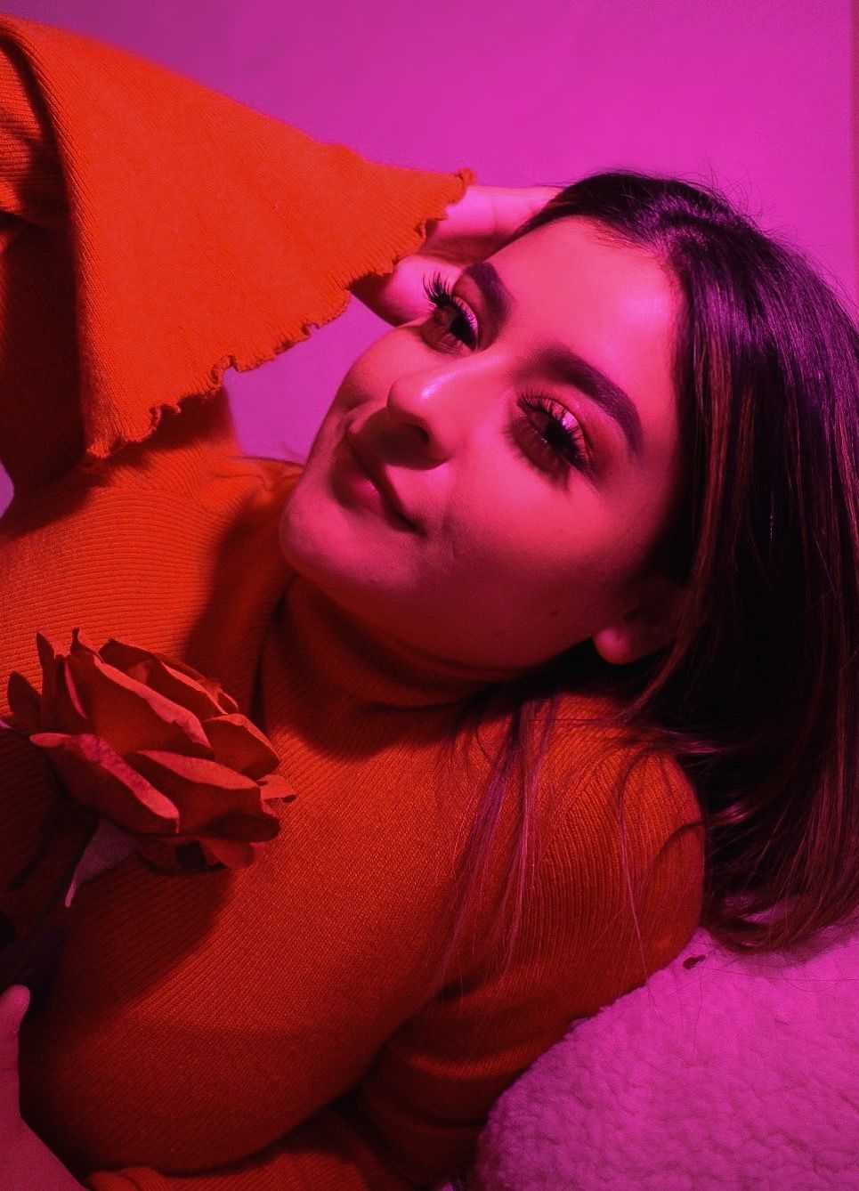 Moody portrait with red rose and sweater against magenta background with dramatic lighting.