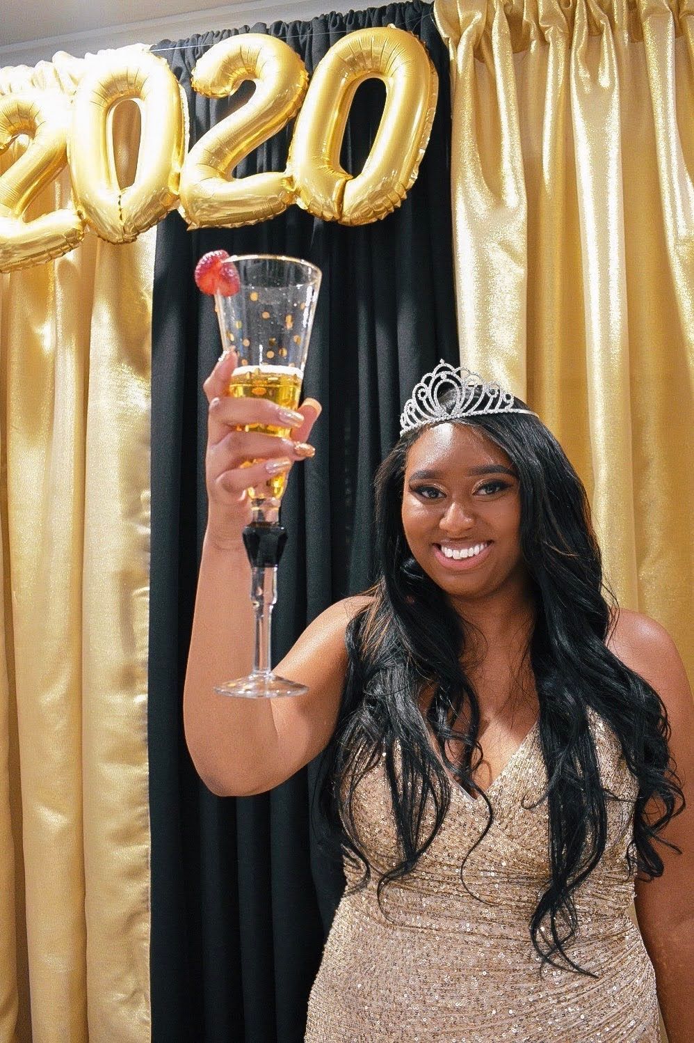 Celebration photo with gold 2020 balloons, champagne glass and sparkling evening gown.