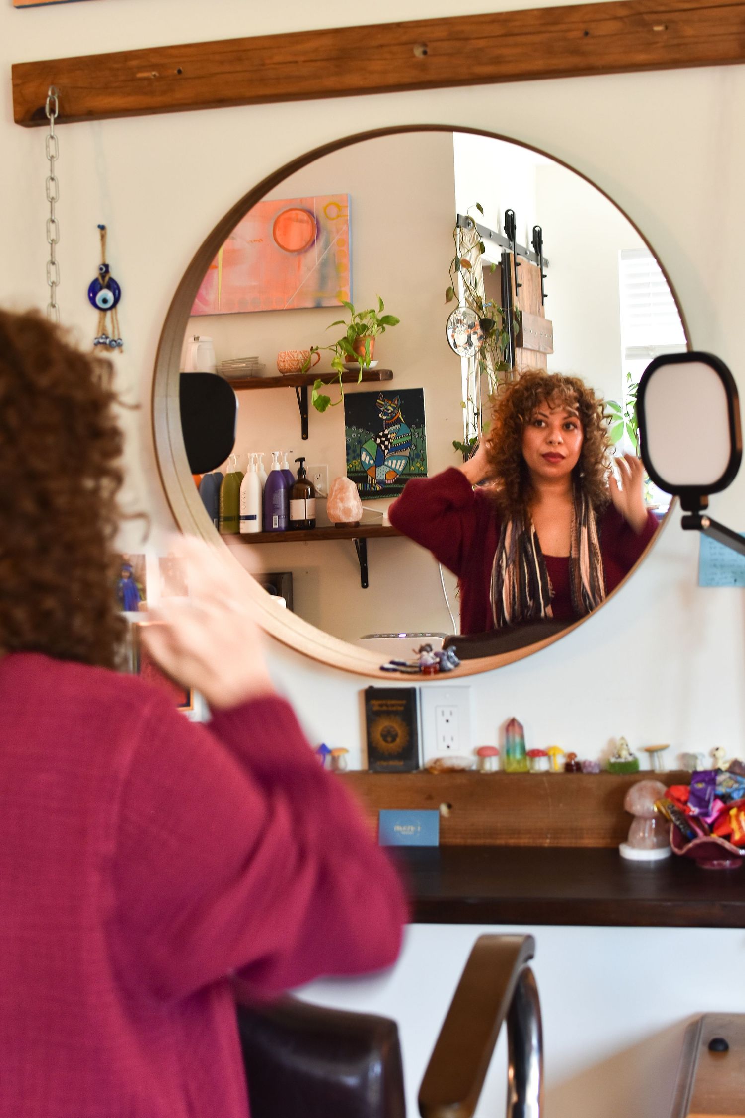 Round mirror reflection in hair salon showing decorative neon sign and shelving with styling products and decor.