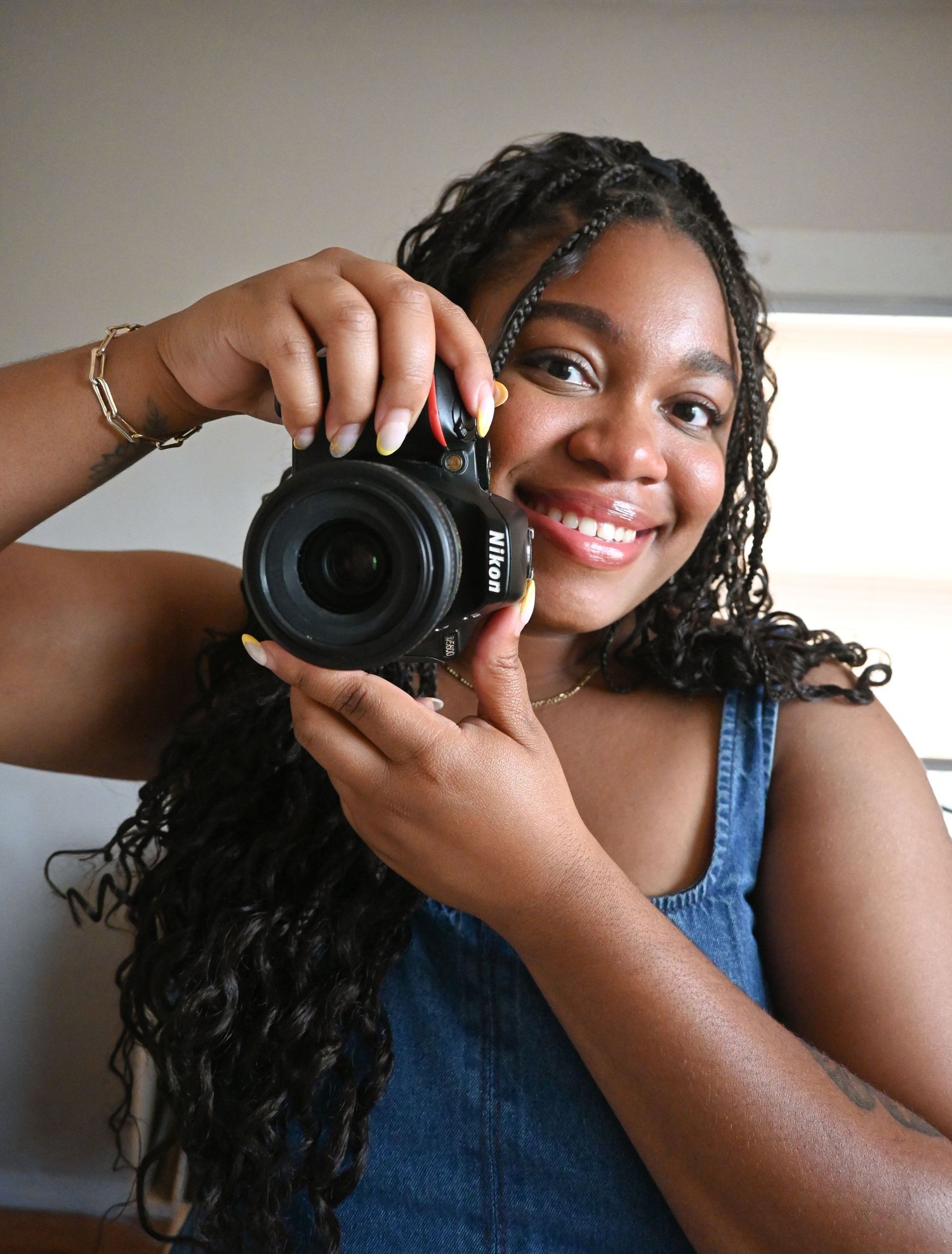 A cheerful photographer captures a self-portrait with a professional camera while wearing a denim top.