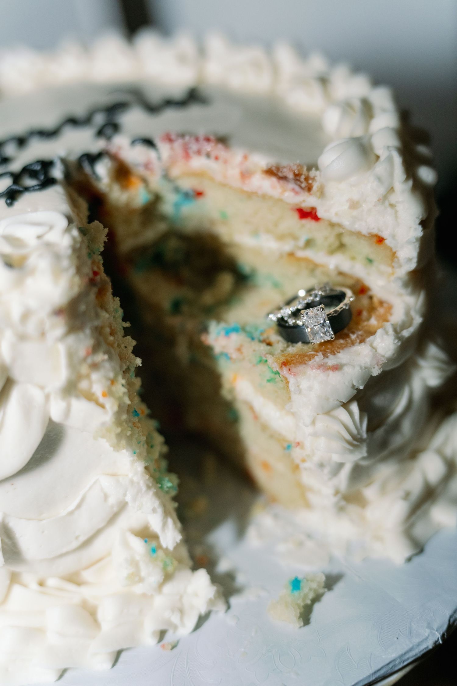 Sliced white wedding cake with confetti sprinkles inside and diamond engagement ring displayed.