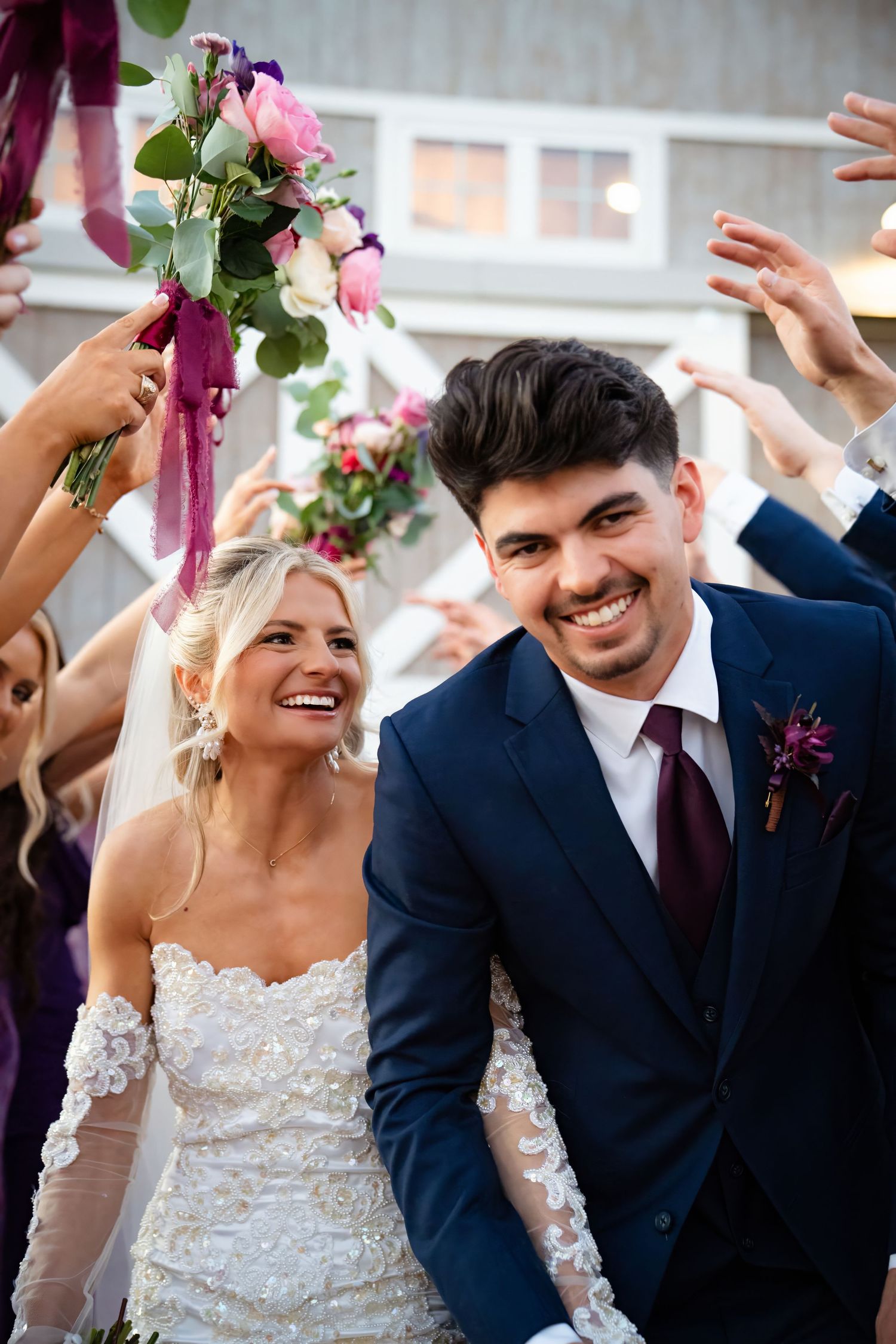 Smiling newlyweds celebrate their recessional as wedding party raises hands and bouquet in joyful send-off.