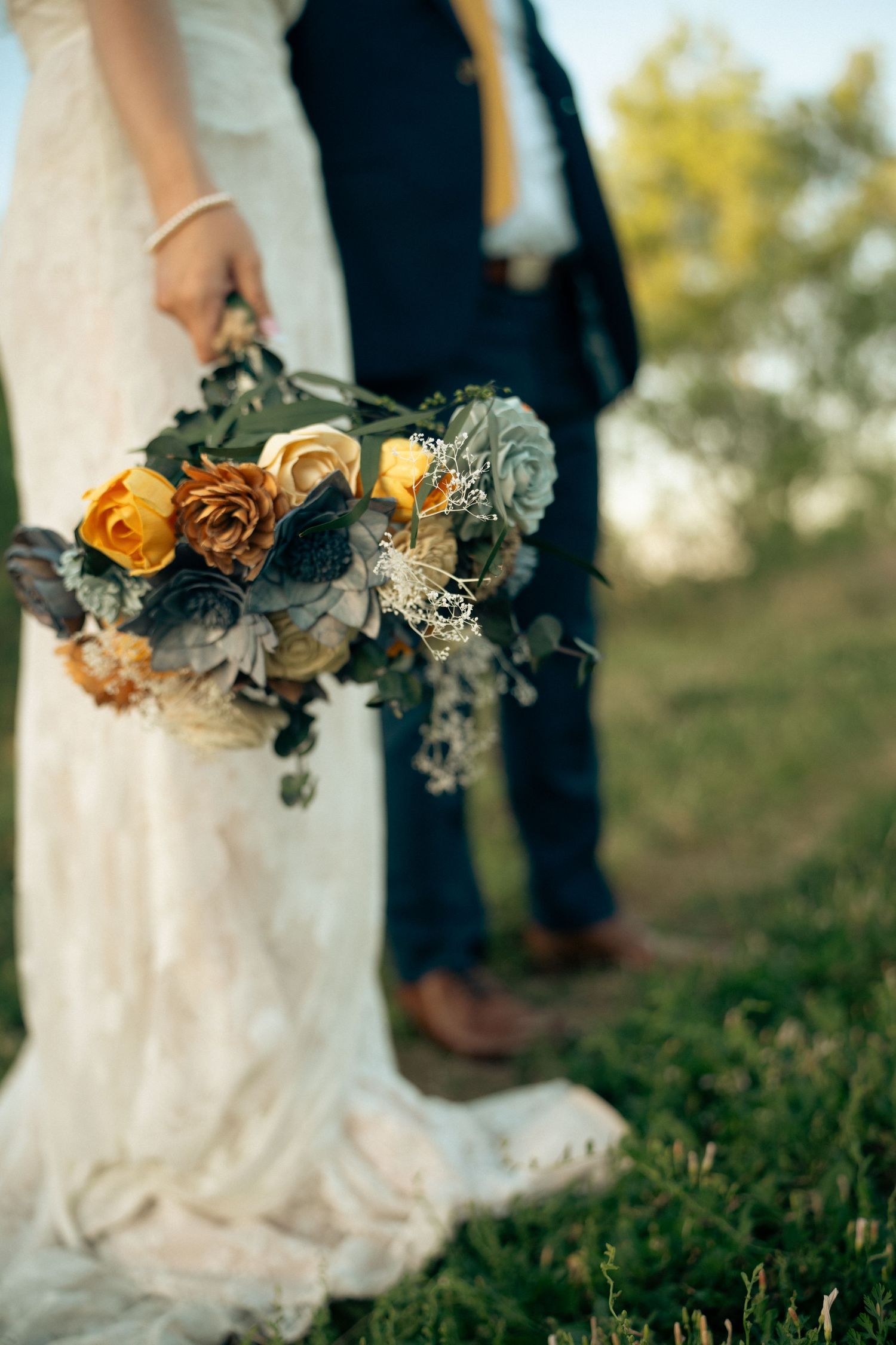 Close-up of bridal bouquet with orange roses, succulents, and greenery held by bride in lace dress.
