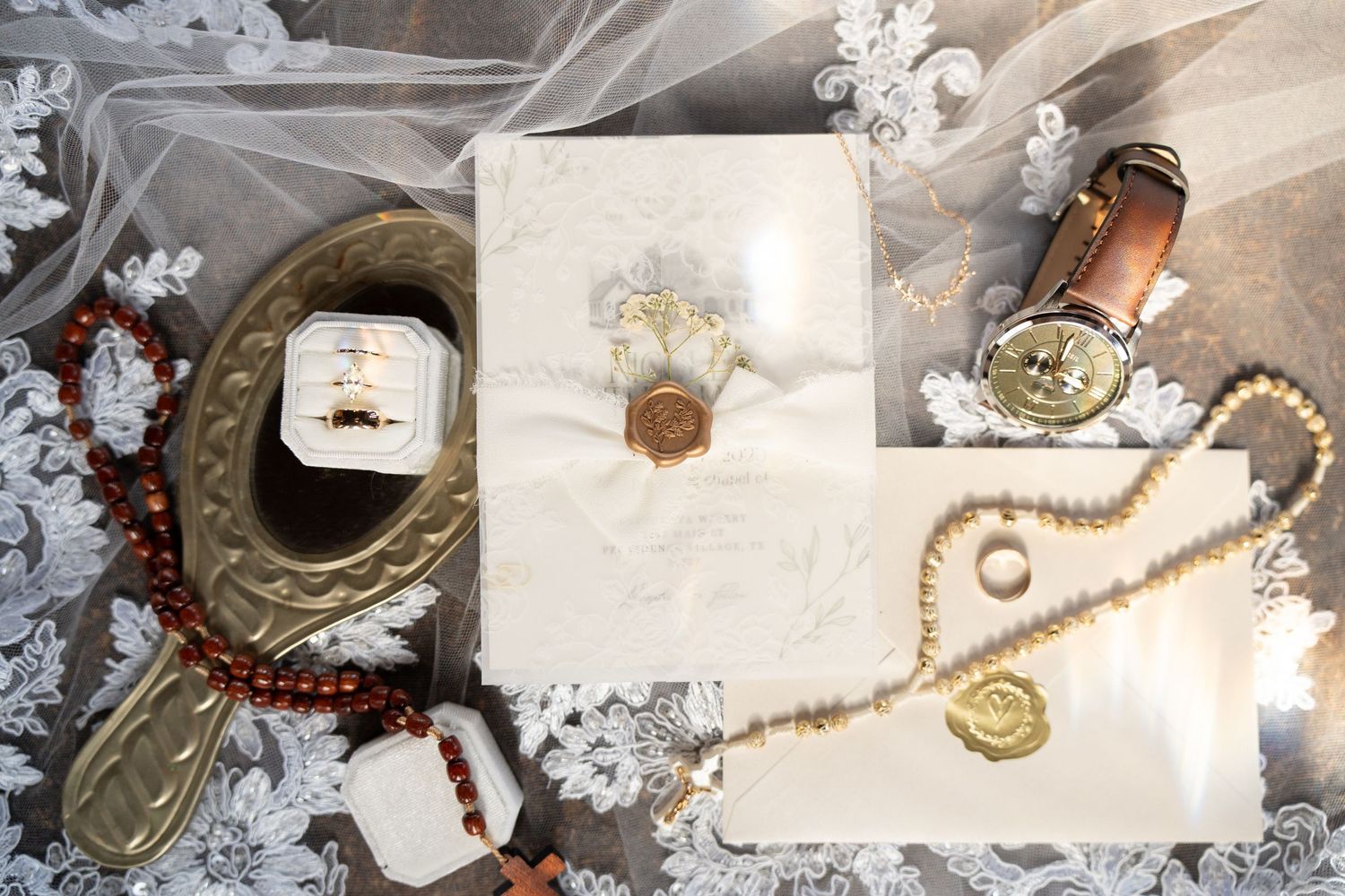 Elegant wedding flat lay featuring gold rings, pearl necklace, wax seal stationery, and vintage mirror on lace veil.