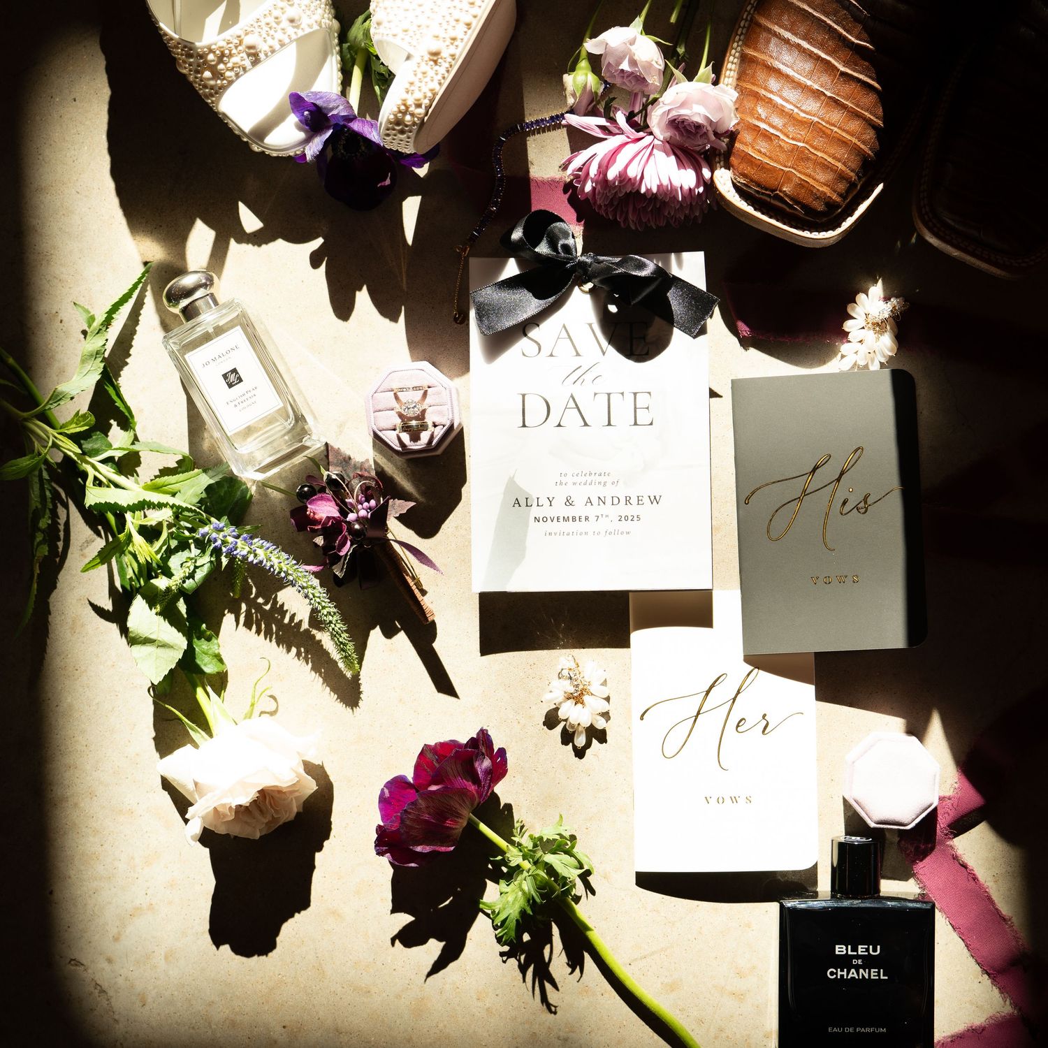 Elegant wedding flat lay featuring save the date cards, perfume, and purple floral accents.