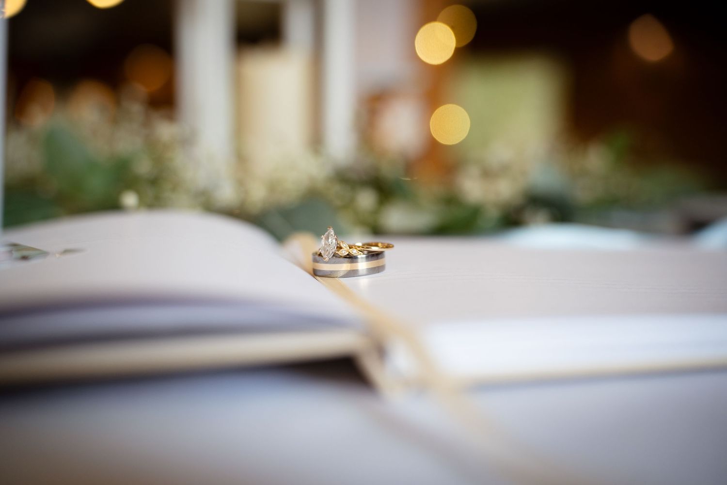 Two gold wedding bands placed on an open book with bokeh lights in the background.