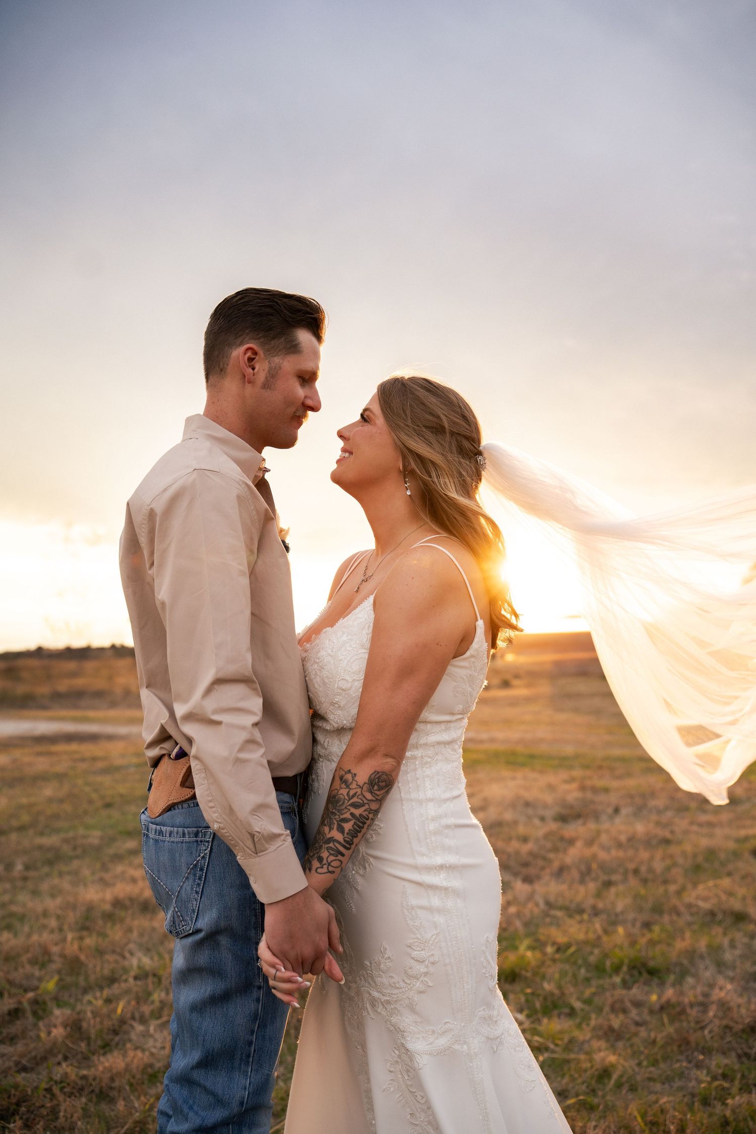Couple shares romantic sunset moment in field with brides veil flowing in the breeze.