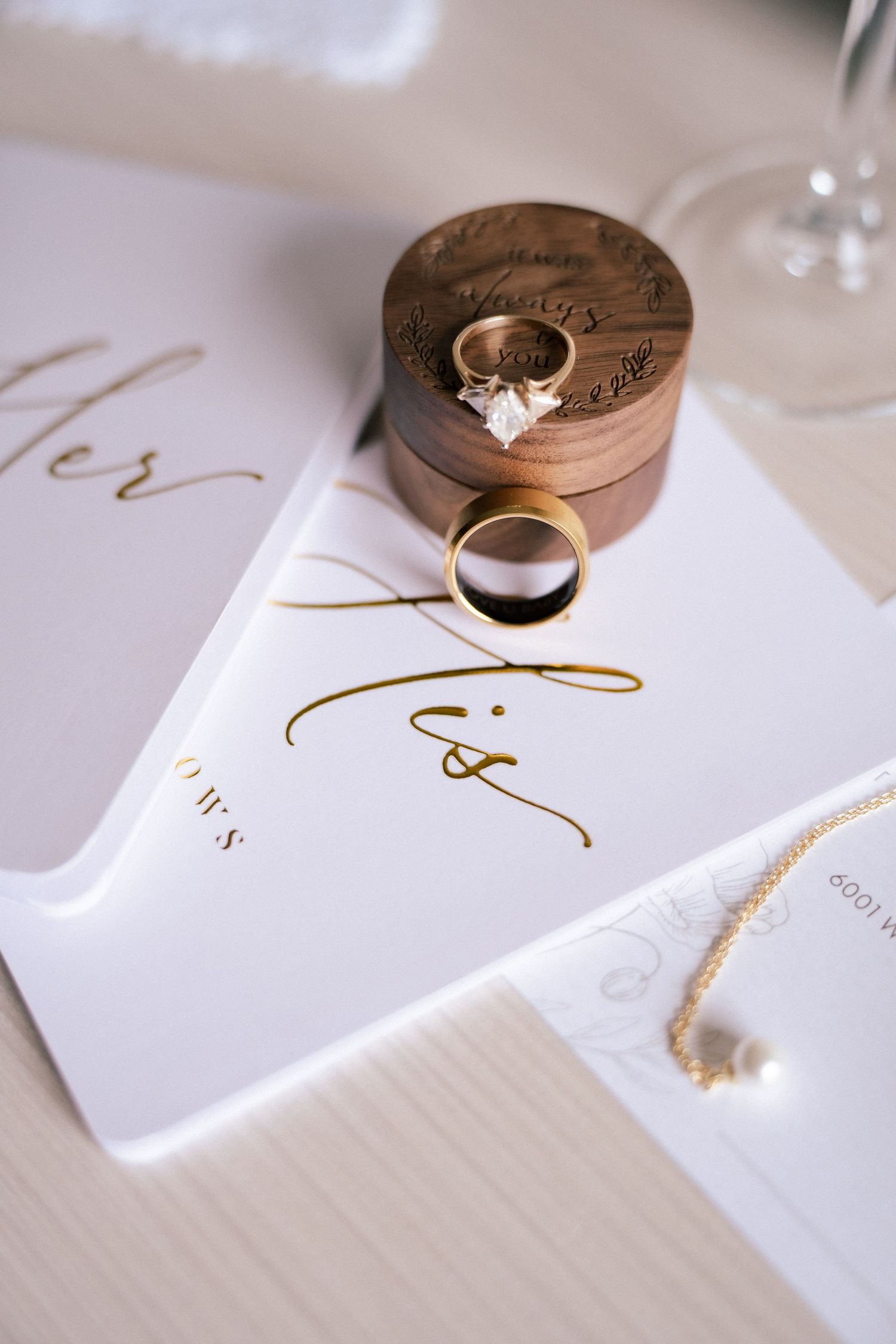 Gold wedding rings and diamond engagement ring displayed on elegant white wedding stationery with gold calligraphy.