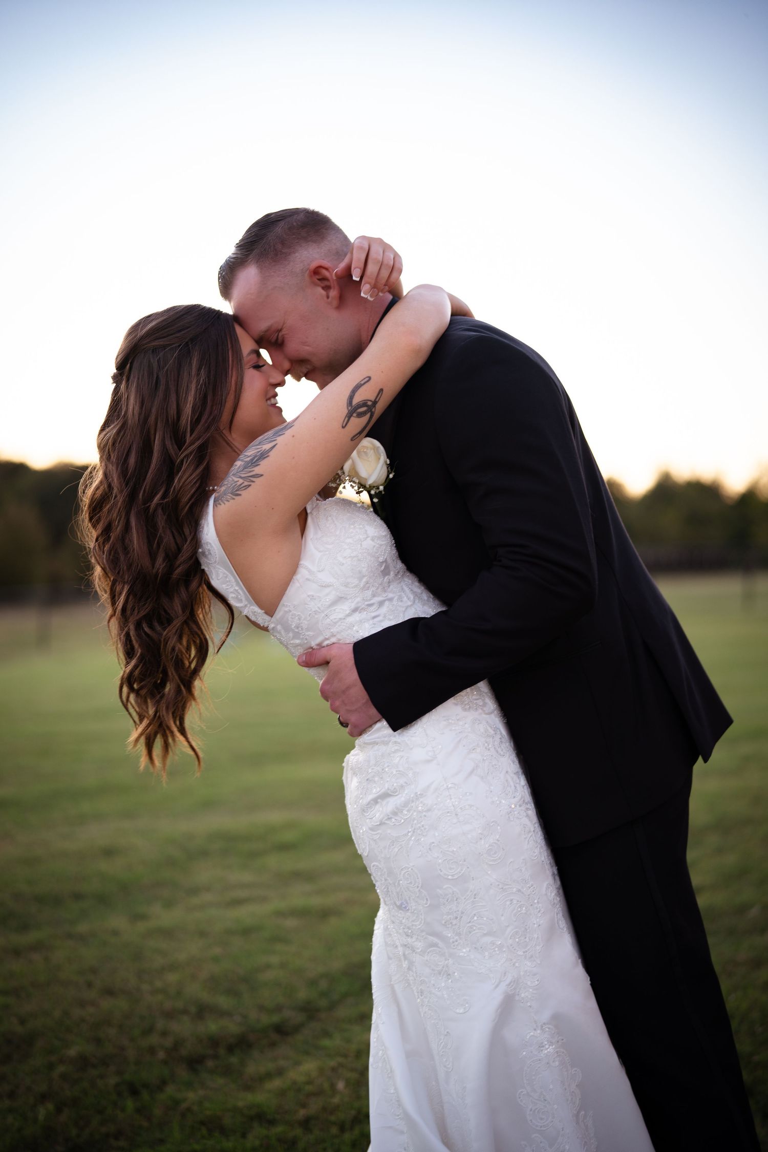 Bride and groom share romantic forehead touch embrace at sunset in open field.