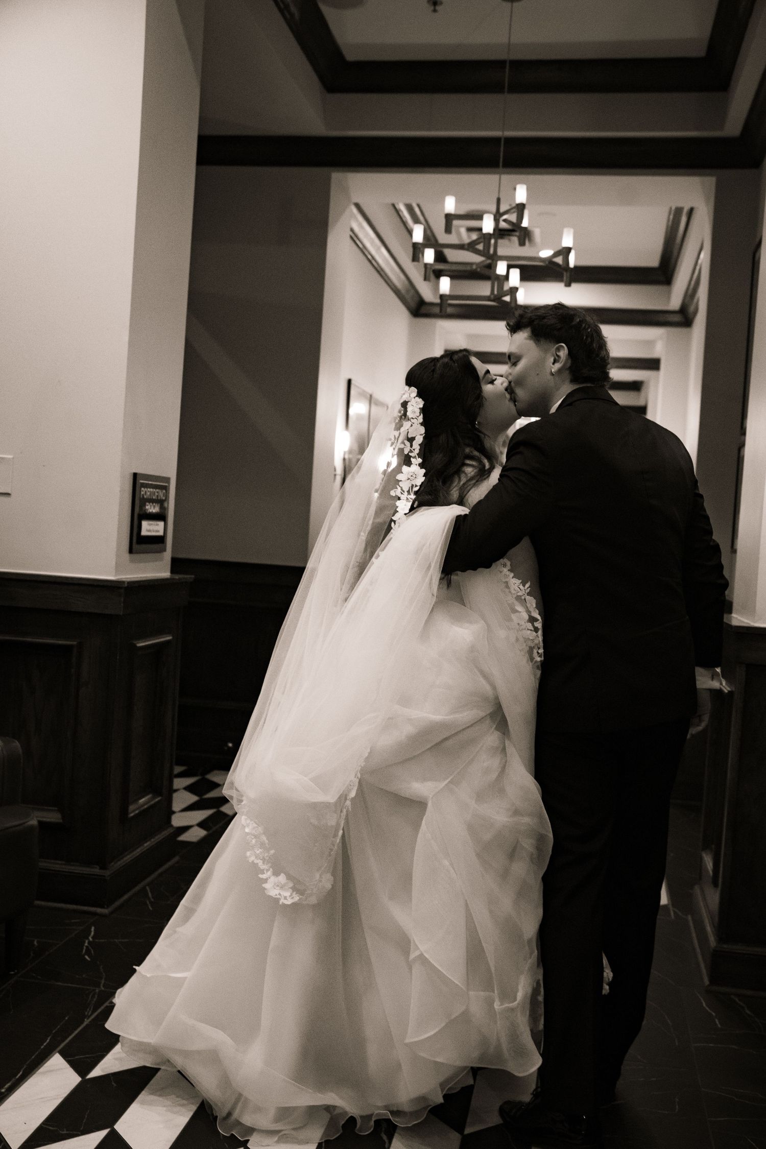 Bride and groom sharing a romantic kiss in a classic black and white hallway portrait.