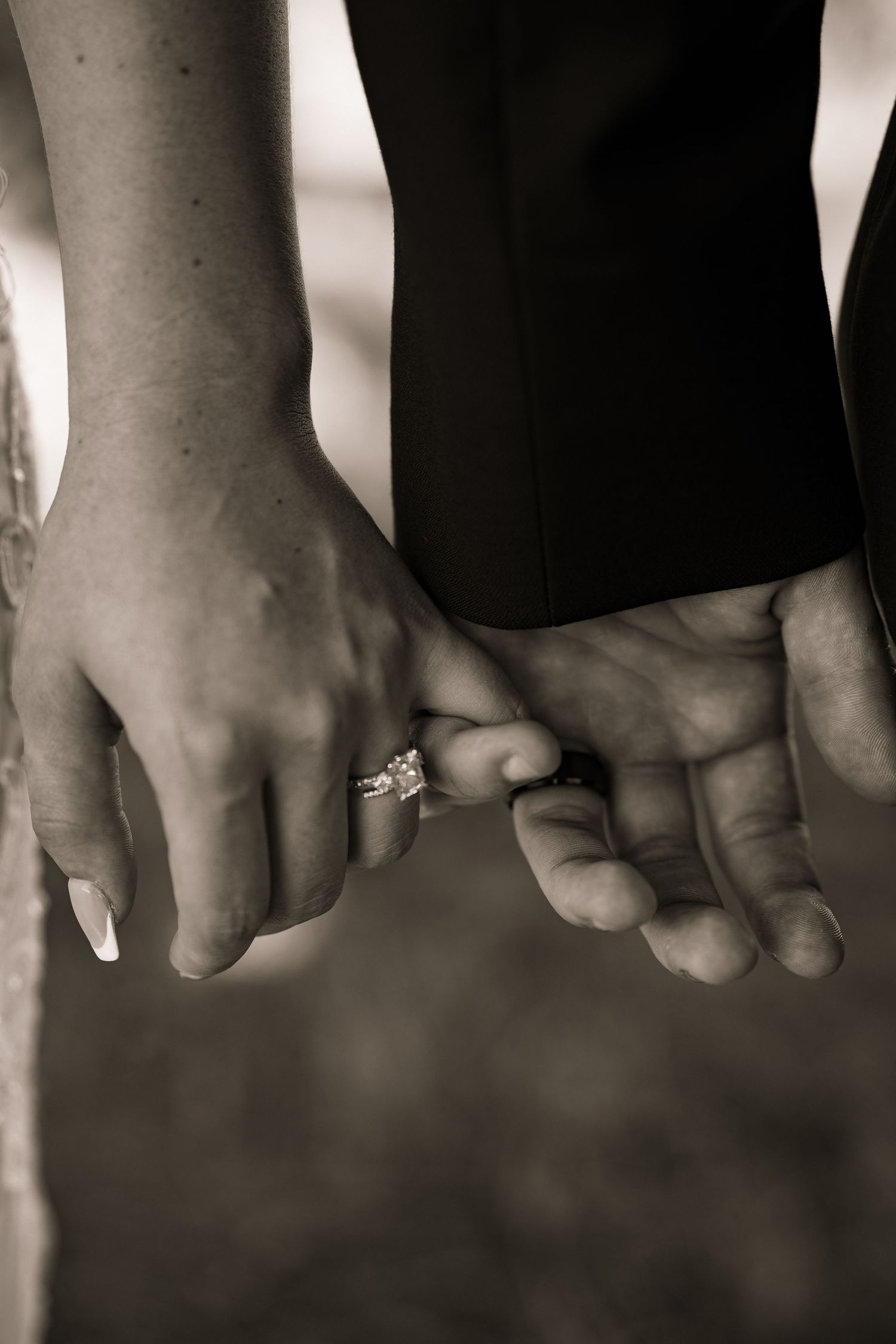 Black and white close-up of bride and groom holding hands with diamond engagement ring visible.